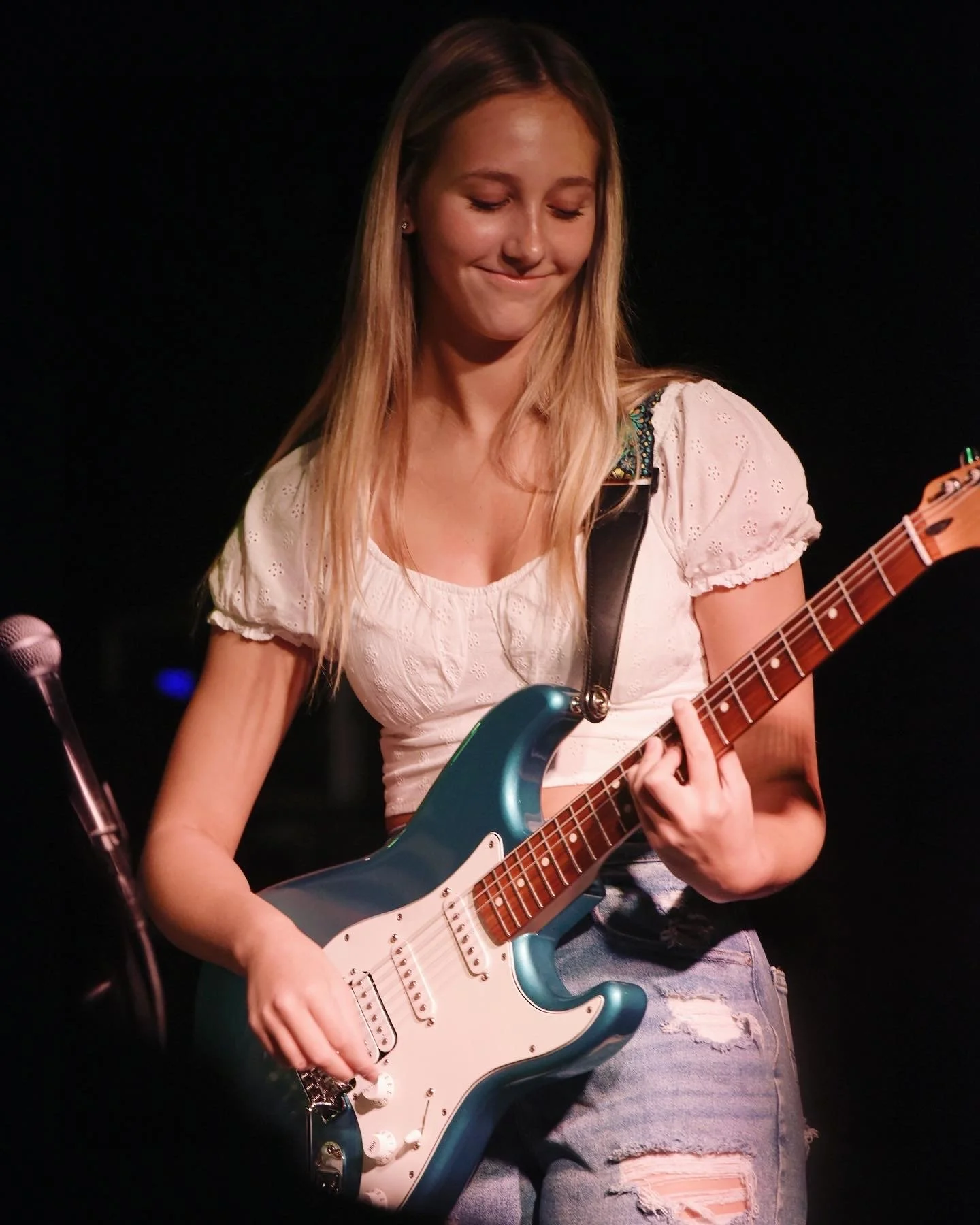 Blonde woman playing a blue electric guitar on a dimly lit stage