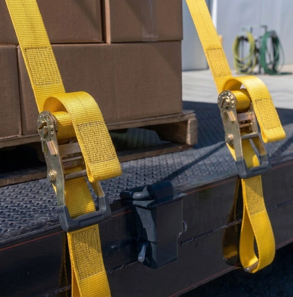Yellow ratchet tie-down straps securing stacked cardboard boxes on a flatbed trailer