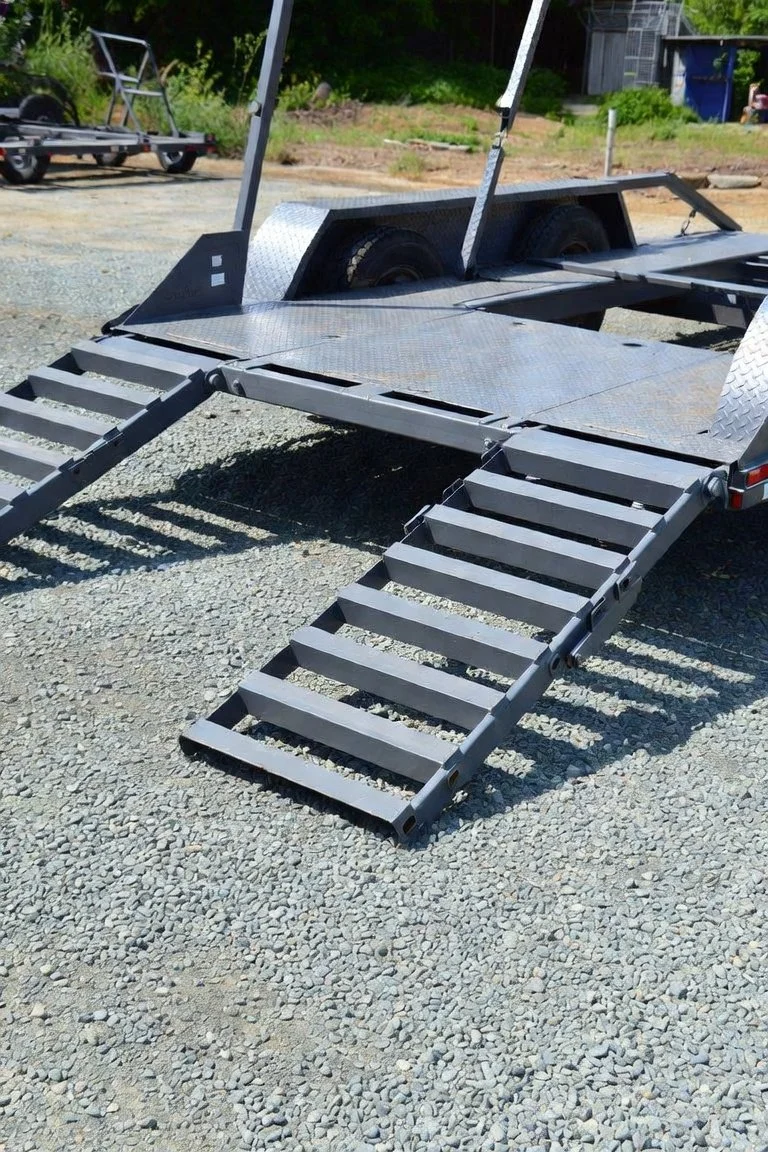 Flatbed utility trailer with dual loading ramps parked on a gravel lot
