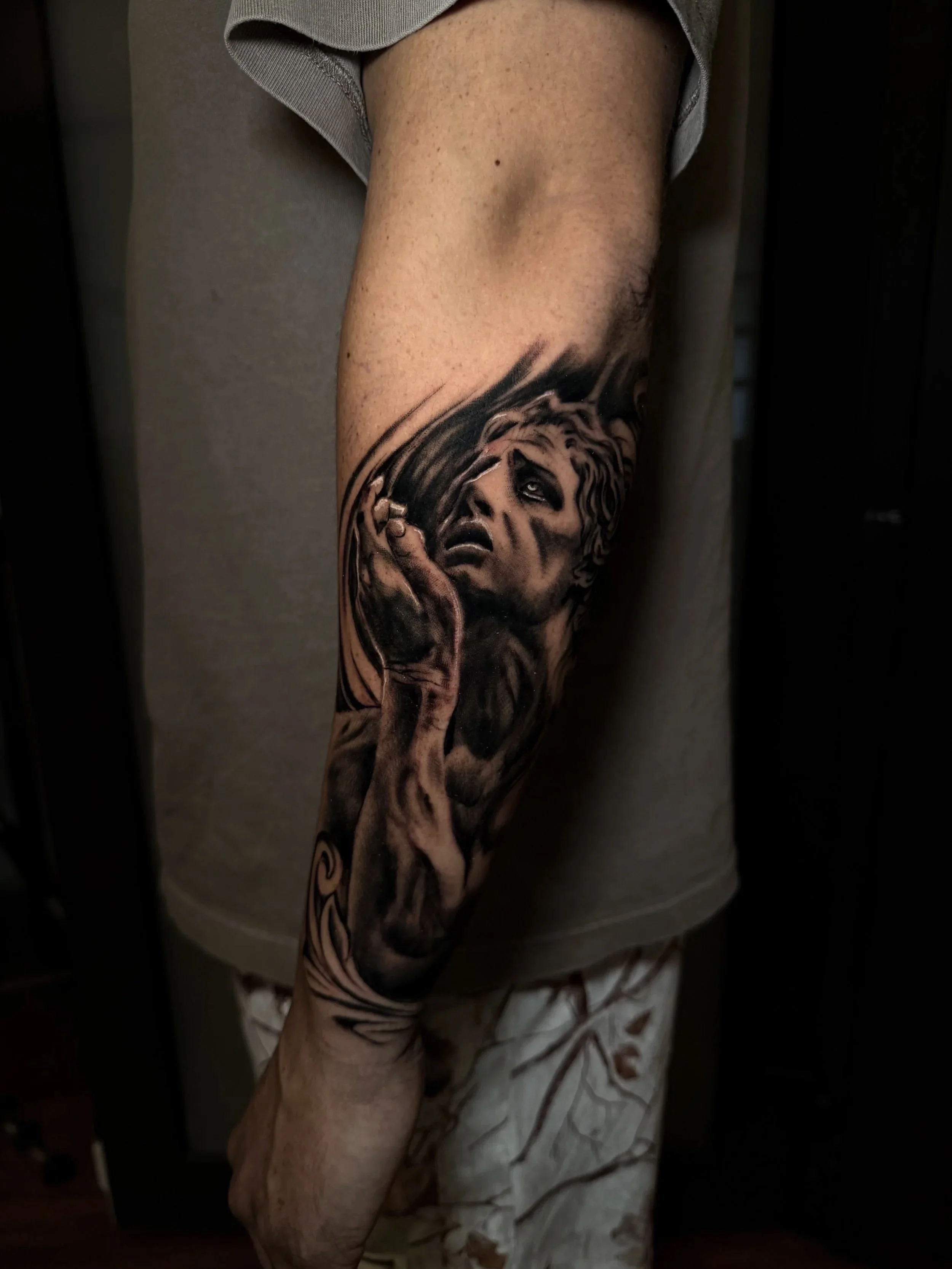 Close-up of a tattooed upper arm featuring a realistic black-and-gray woman’s face with hands covering her mouth.