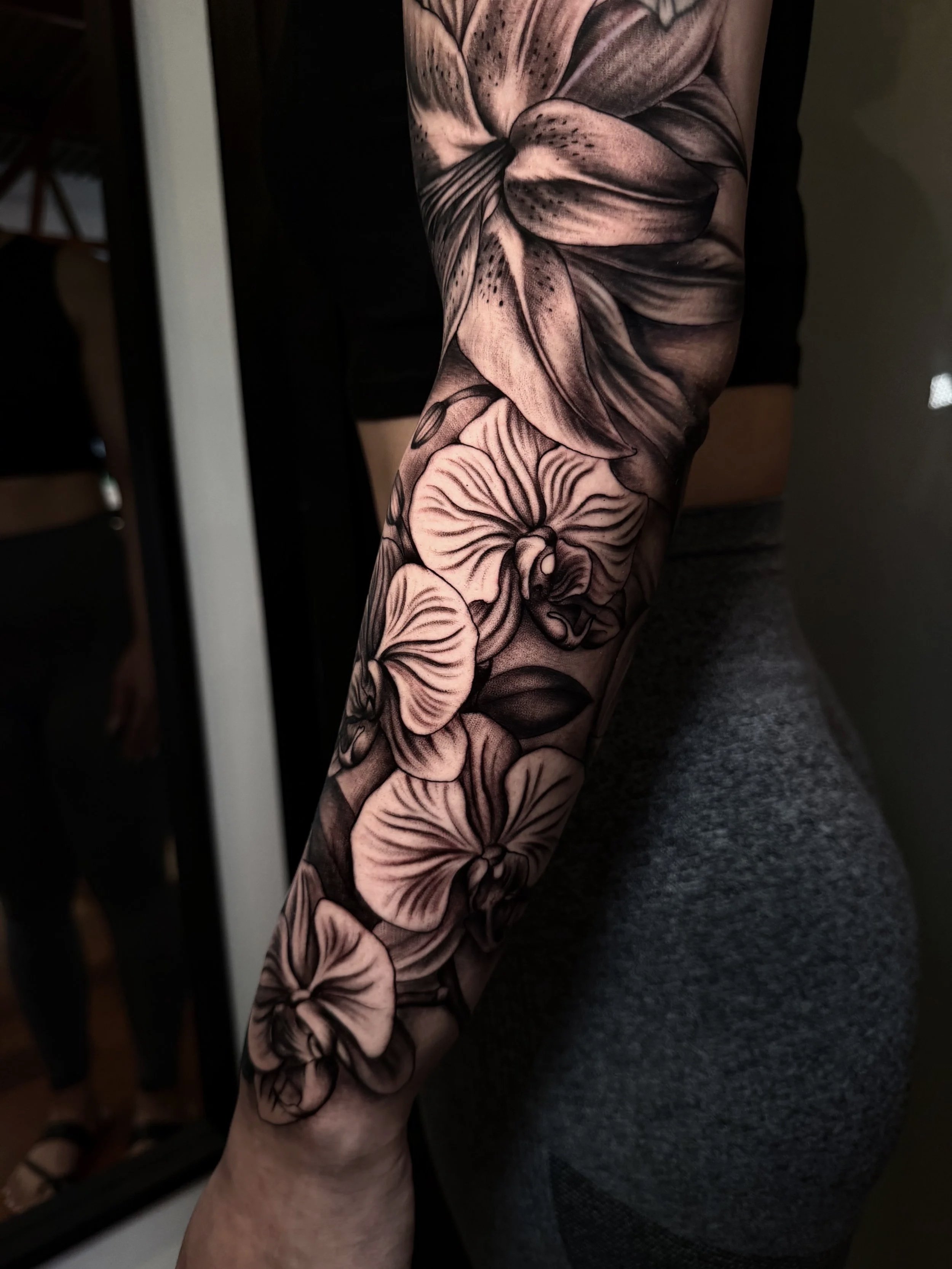 Close-up of a person’s arm with a detailed black-and-gray floral tattoo sleeve