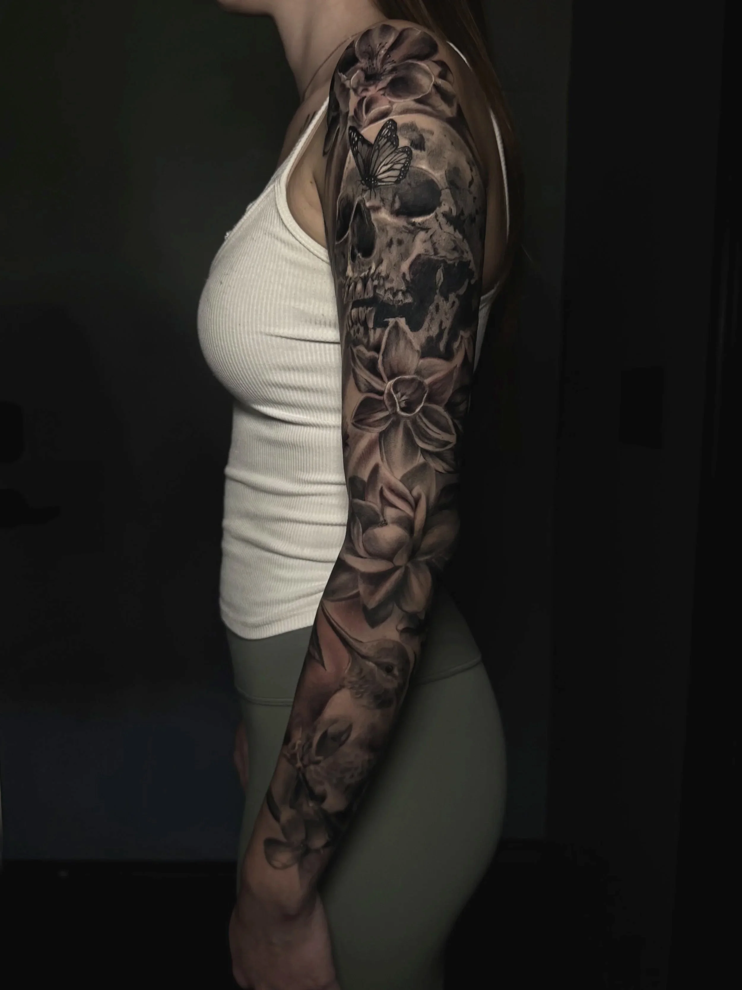 Close-up of an arm with a detailed black-and-gray skull, butterfly, and floral sleeve tattoo.
