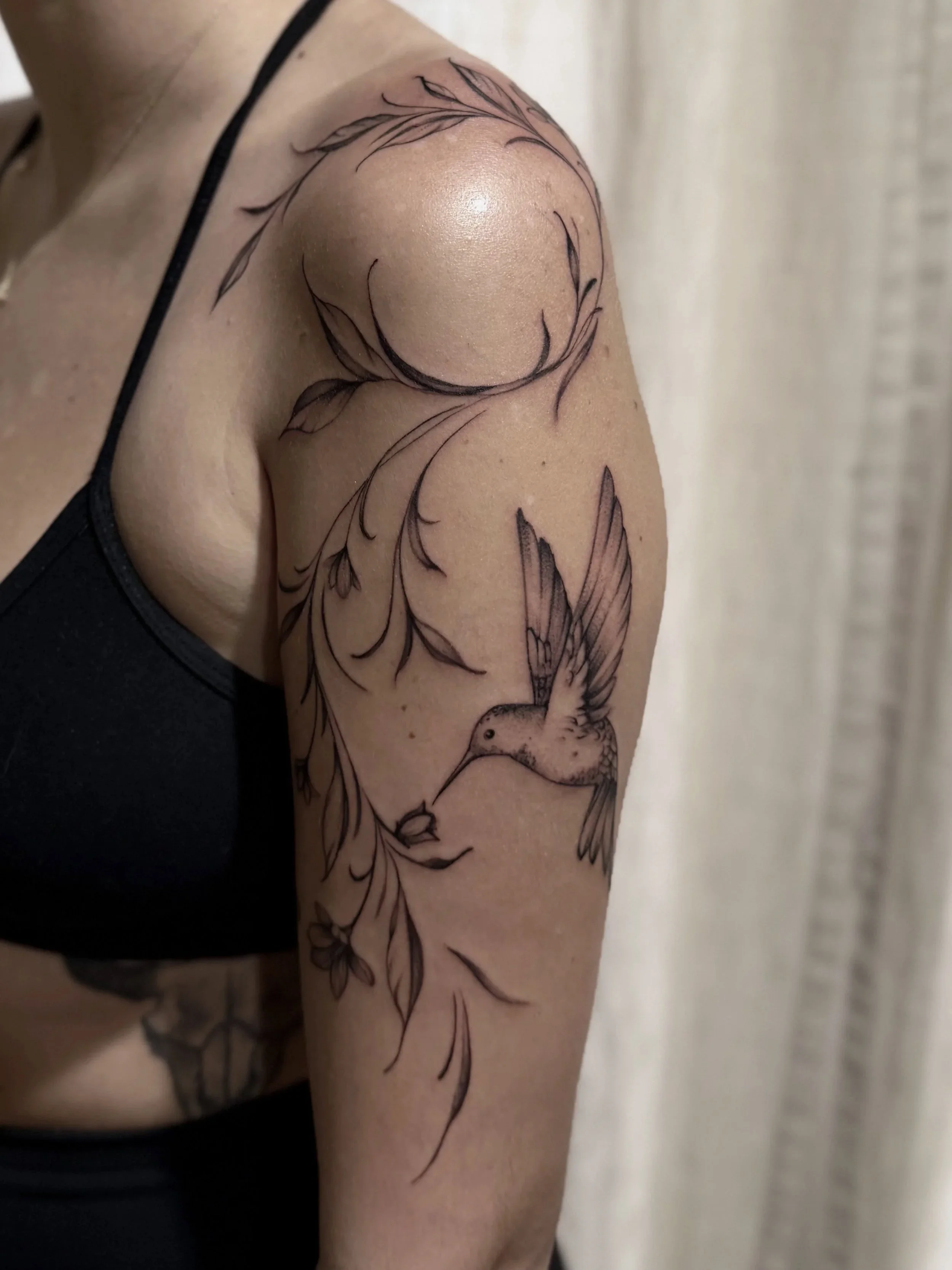 Close-up of a person's upper arm featuring a detailed black-and-gray floral tattoo with a large flower and butterfly.