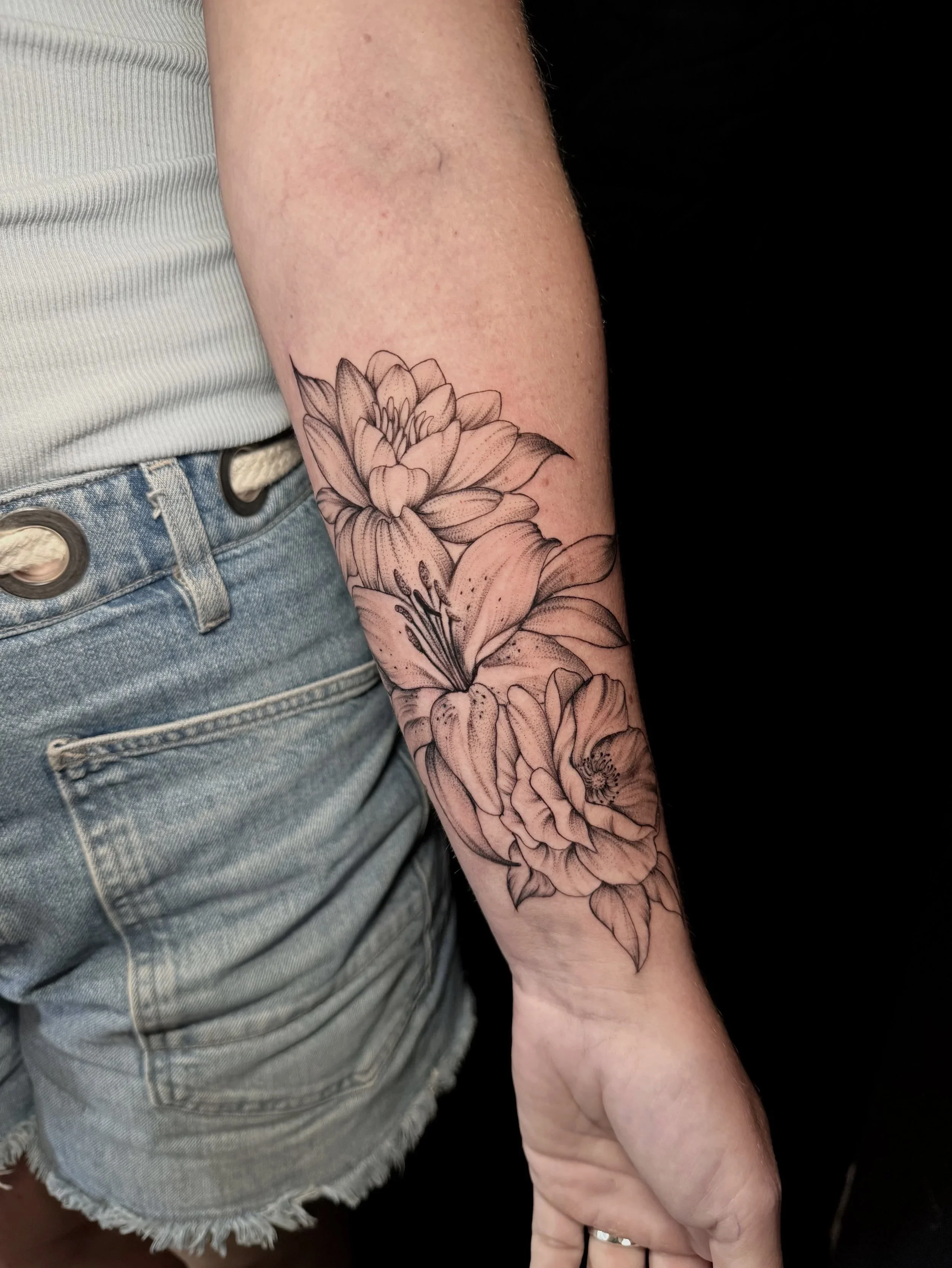Close-up of a forearm featuring a detailed black-and-gray floral tattoo with large layered flowers and leaves.