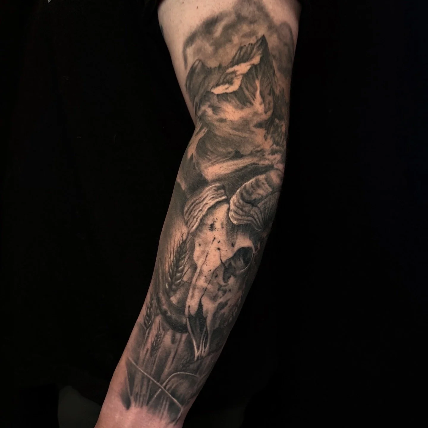 Black-and-gray full-sleeve tattoo featuring a detailed skull, skeletal hands, and dark gothic imagery on an arm.