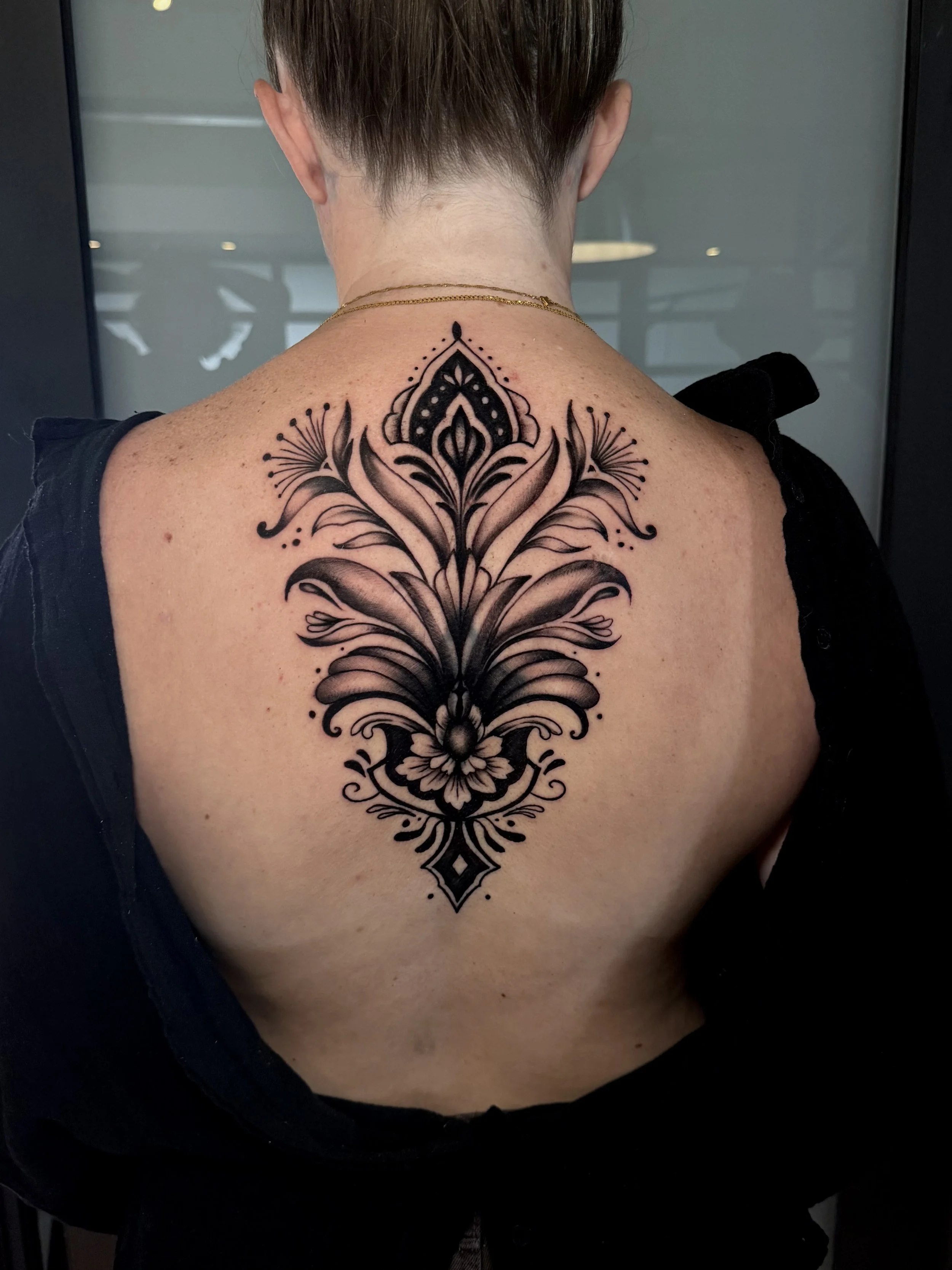Back view of a person showing a large black floral and ornamental tattoo spanning the upper and mid-back.