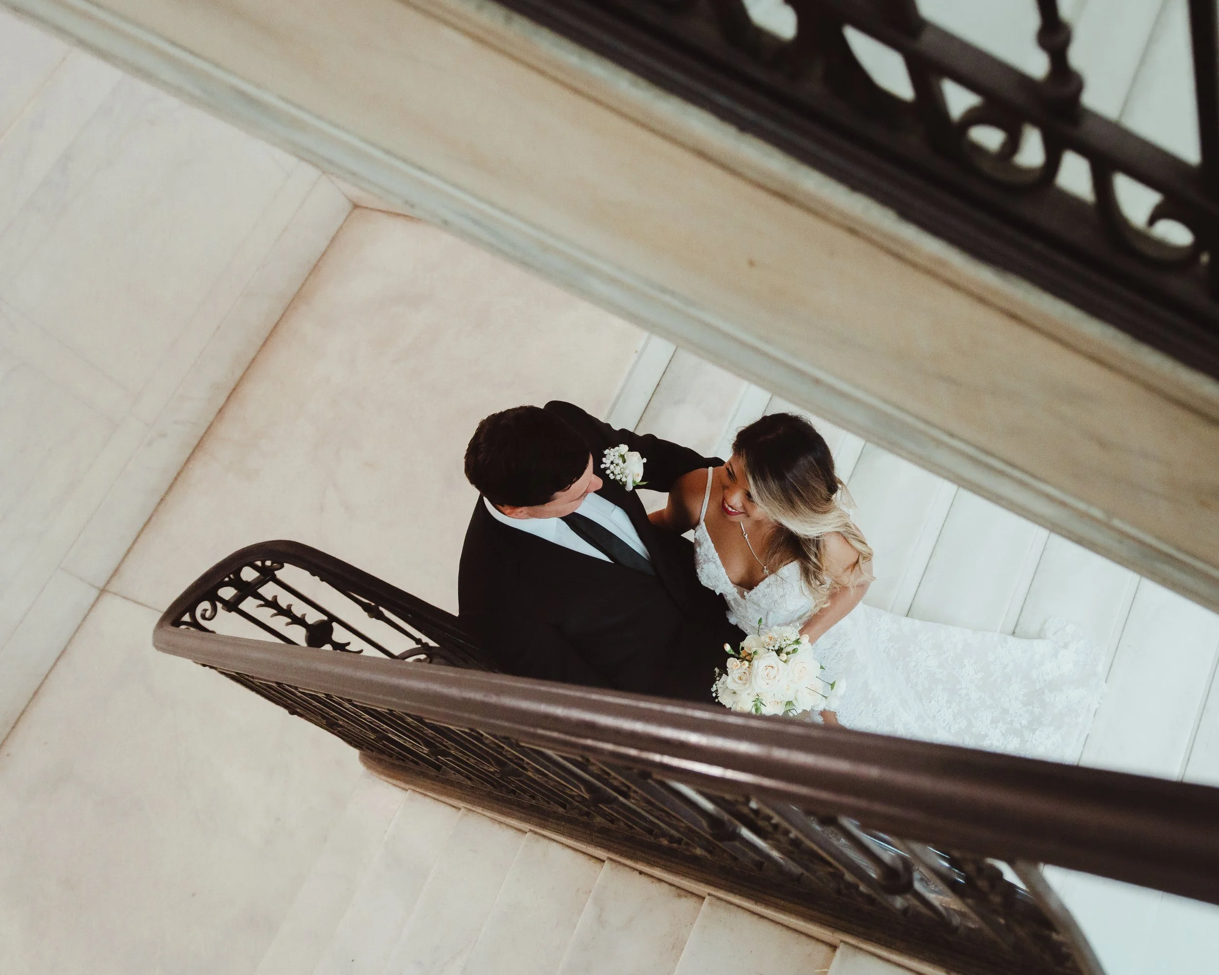Overhead wedding portrait of a bride and groom embracing on a staircase, with the bride holding a white flower bouquet