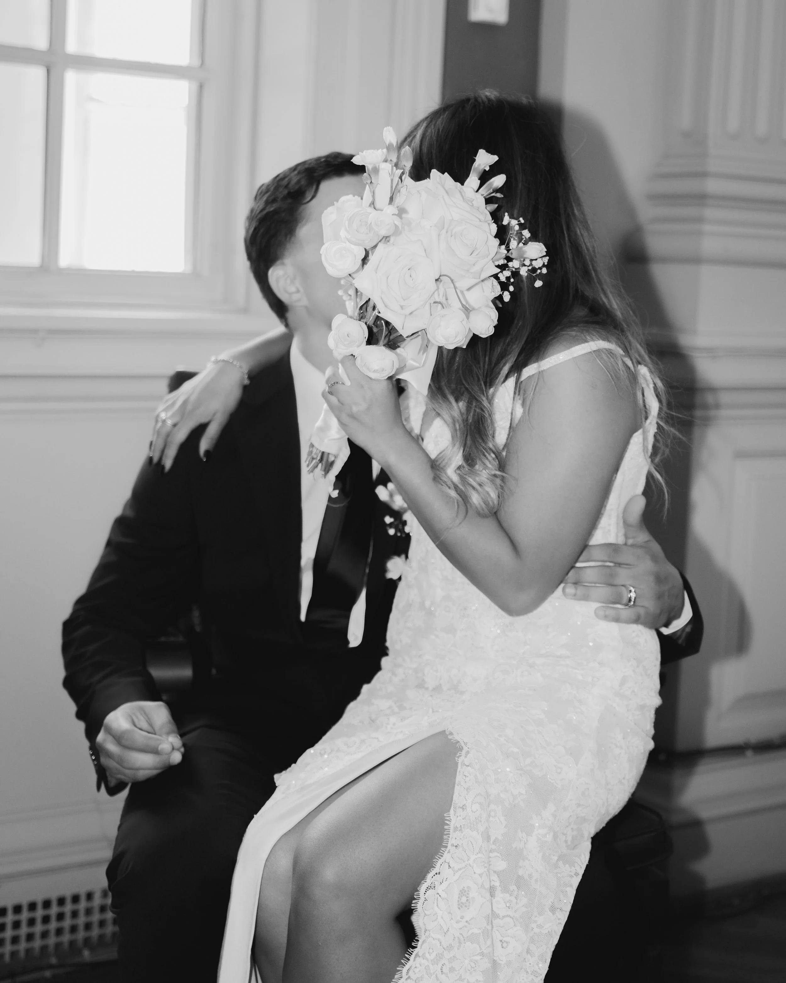 Black-and-white wedding photo of a bride holding a bouquet as she embraces the groom.