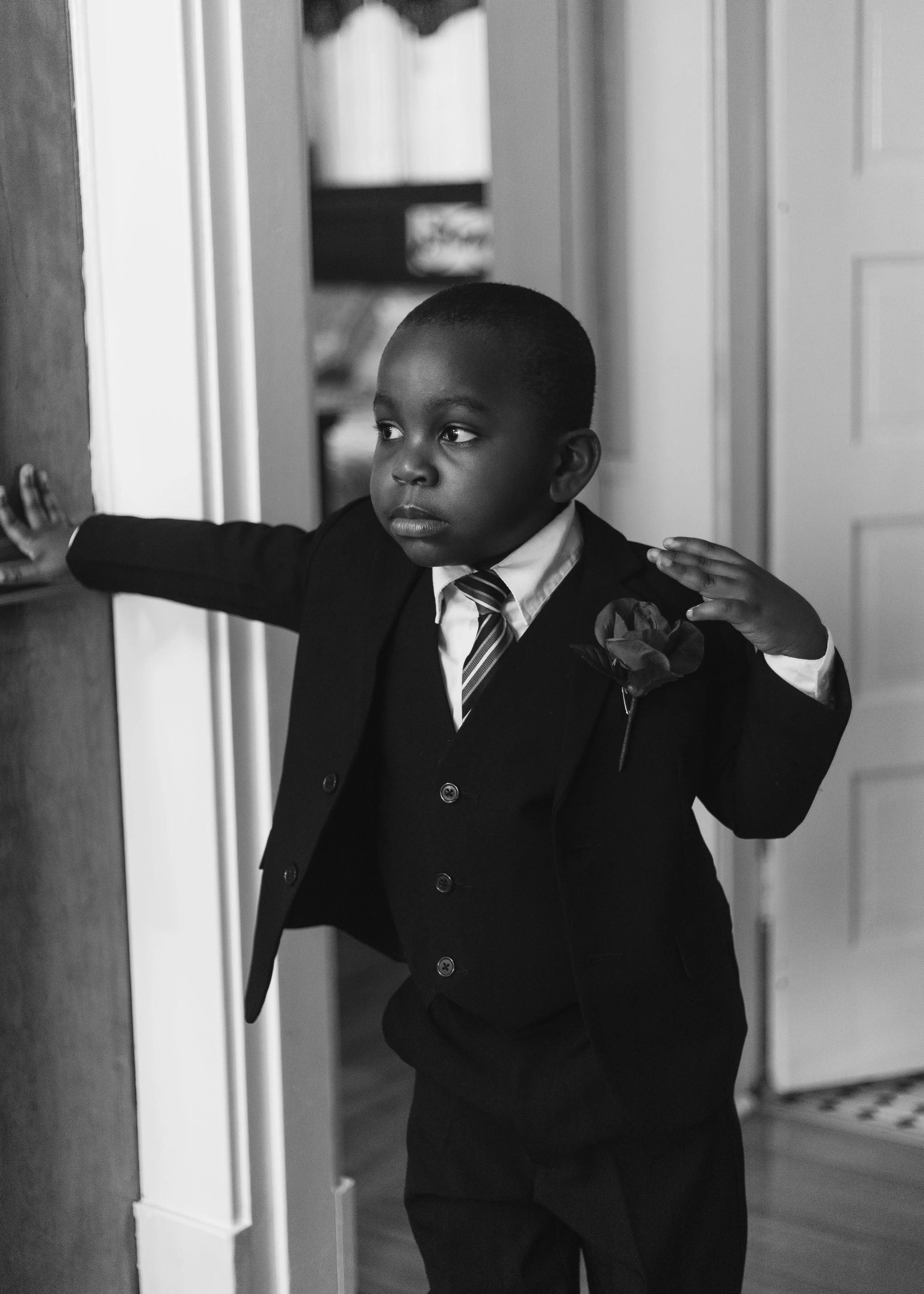 Black-and-white portrait of a young boy in a suit and striped tie adjusting his jacket in a doorway