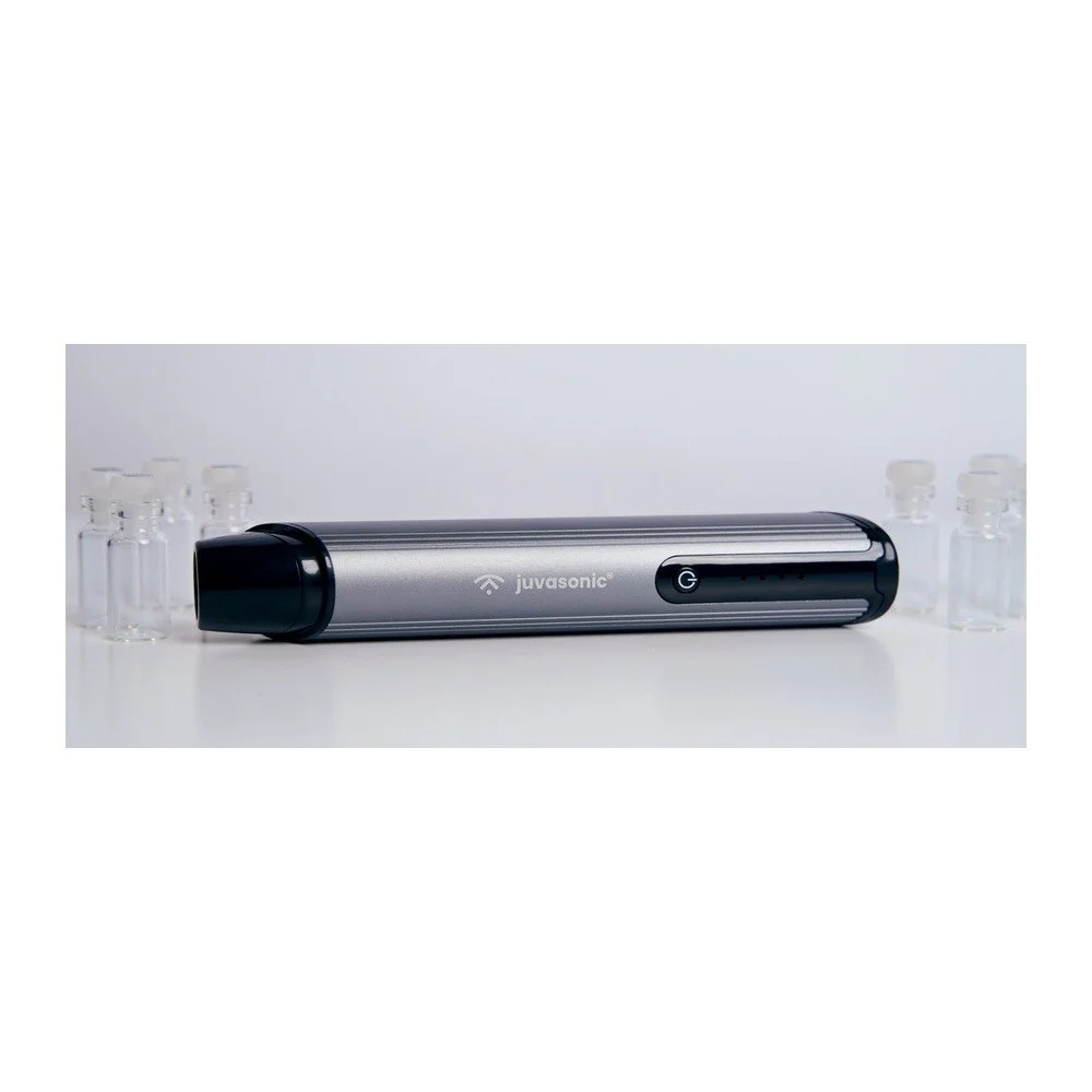 JuvaSonic handheld facial cleansing device displayed with glass bottles