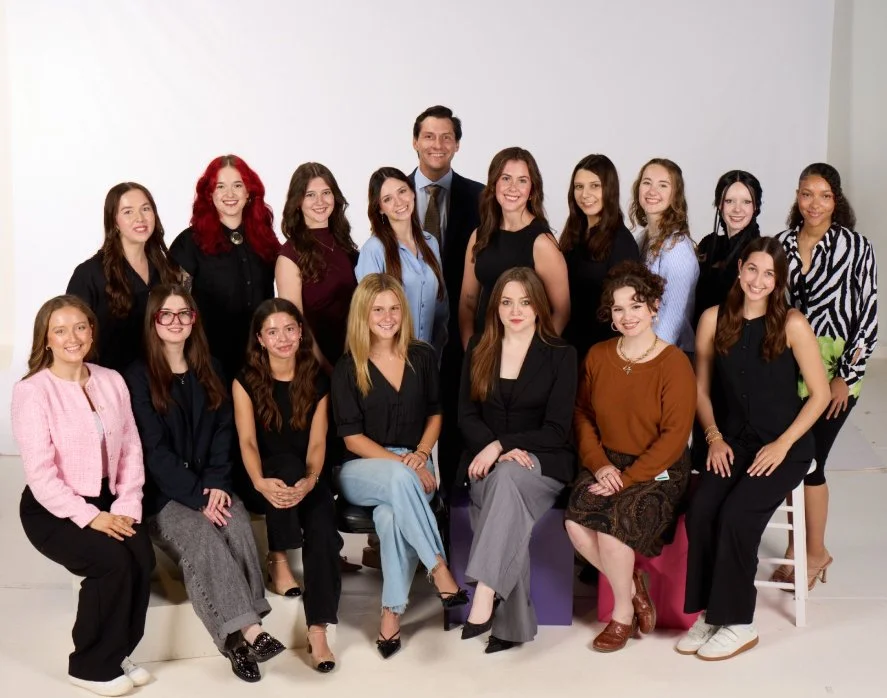 Professional group portrait of 15 diverse adults posing in two rows against a white studio background.