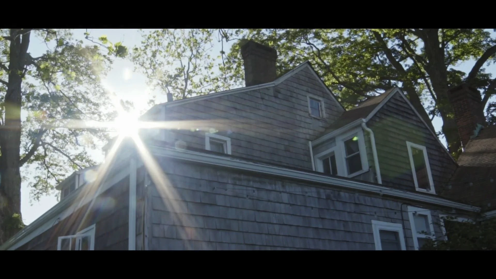 Sunlight behind a shingled farmhouse among tall trees, still from Finding Time, a film for Space on Ryder Farm