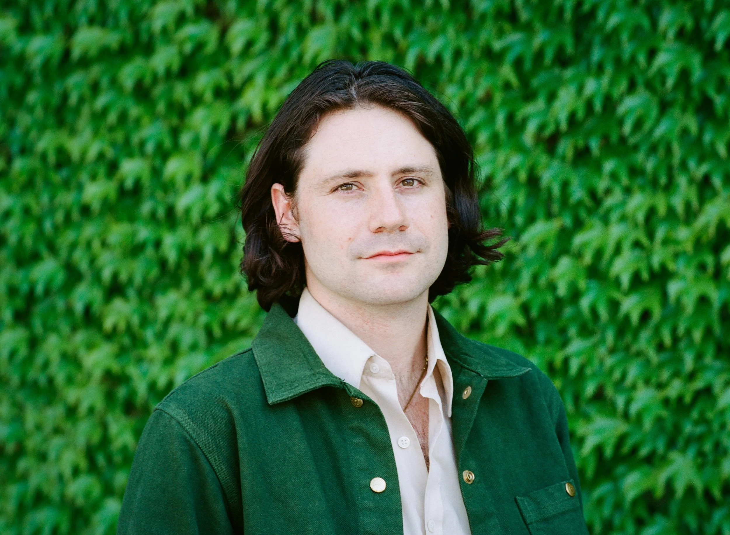Portrait of Brooklyn filmmaker Grant Conversano in a green jacket against a wall of ivy