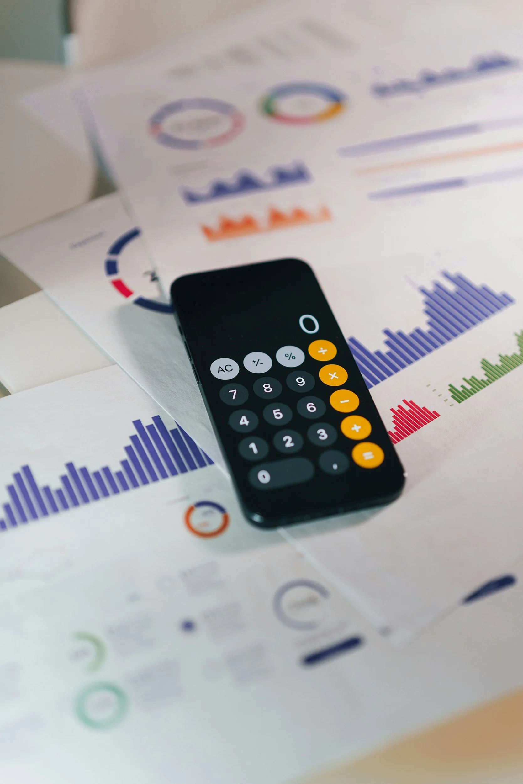 Smartphone calculator on printed financial reports with colorful charts and graphs