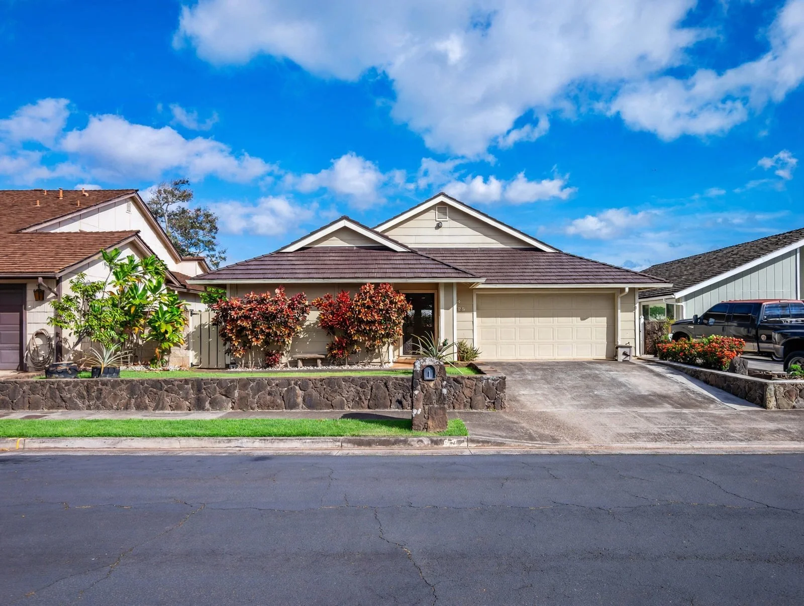 Single-story Oahu home with a driveway, lawn, and flowering shrubs under a blue sky
