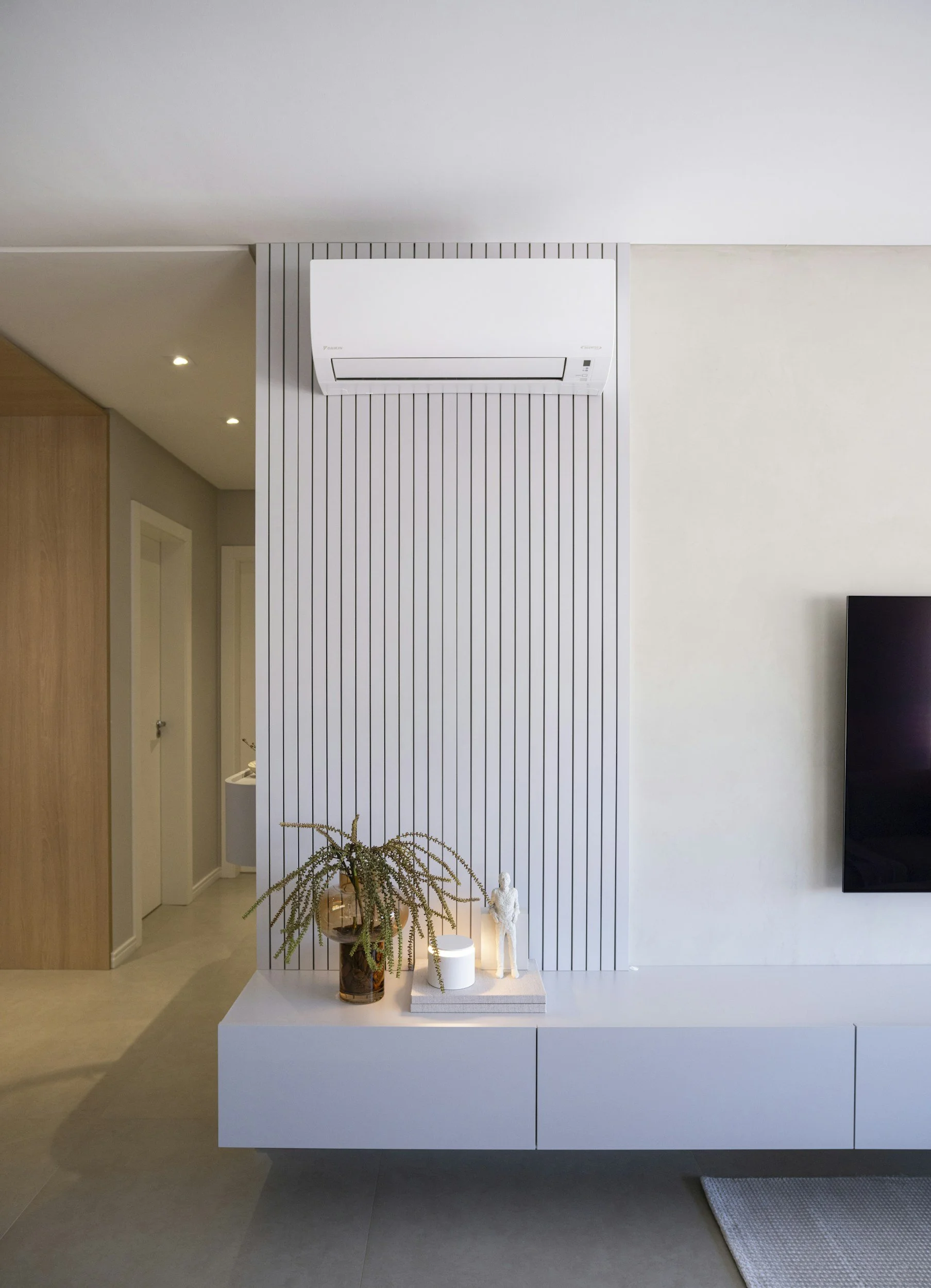 Salon moderne avec climatiseur mural, meuble blanc, plante décorative et télévision.
