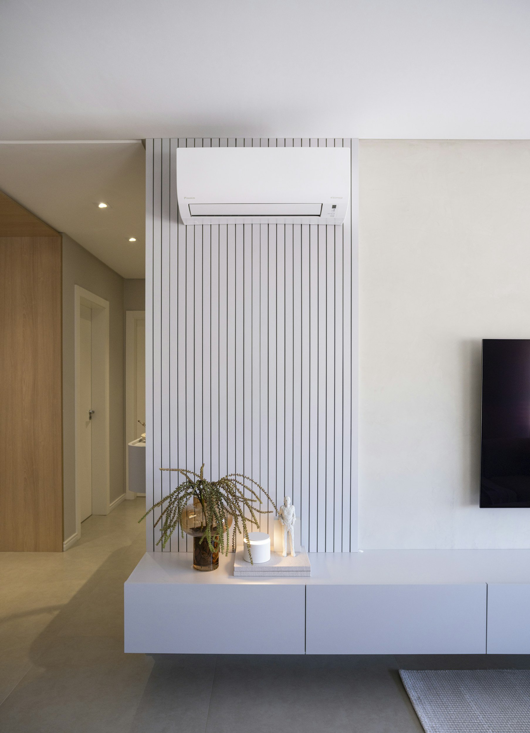 Salon moderne avec climatiseur mural, meuble TV blanc, plante décorative et télévision à écran plat.