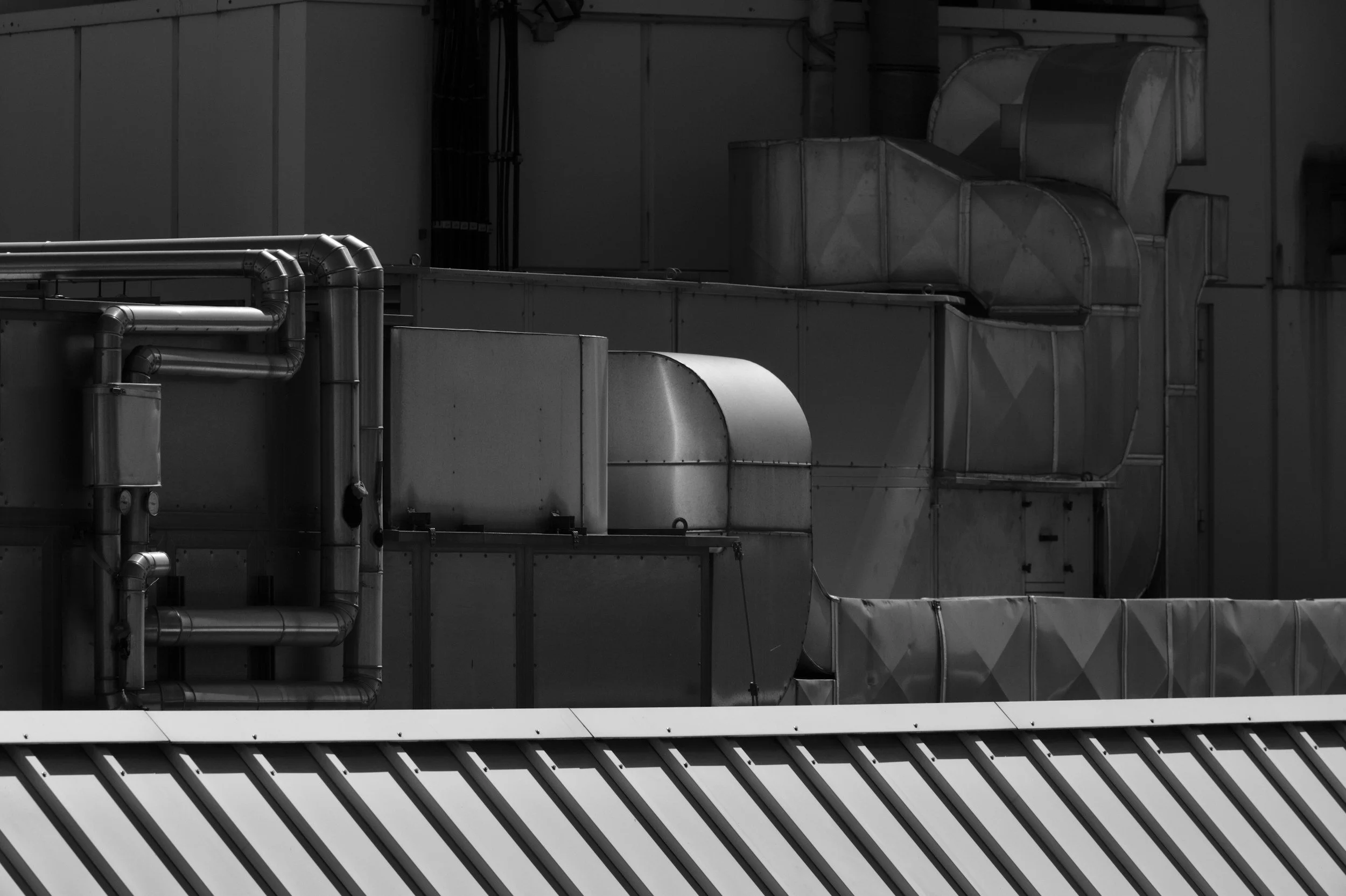 Conduits et gaines de ventilation industrielles sur le toit d’un bâtiment, en noir et blanc.