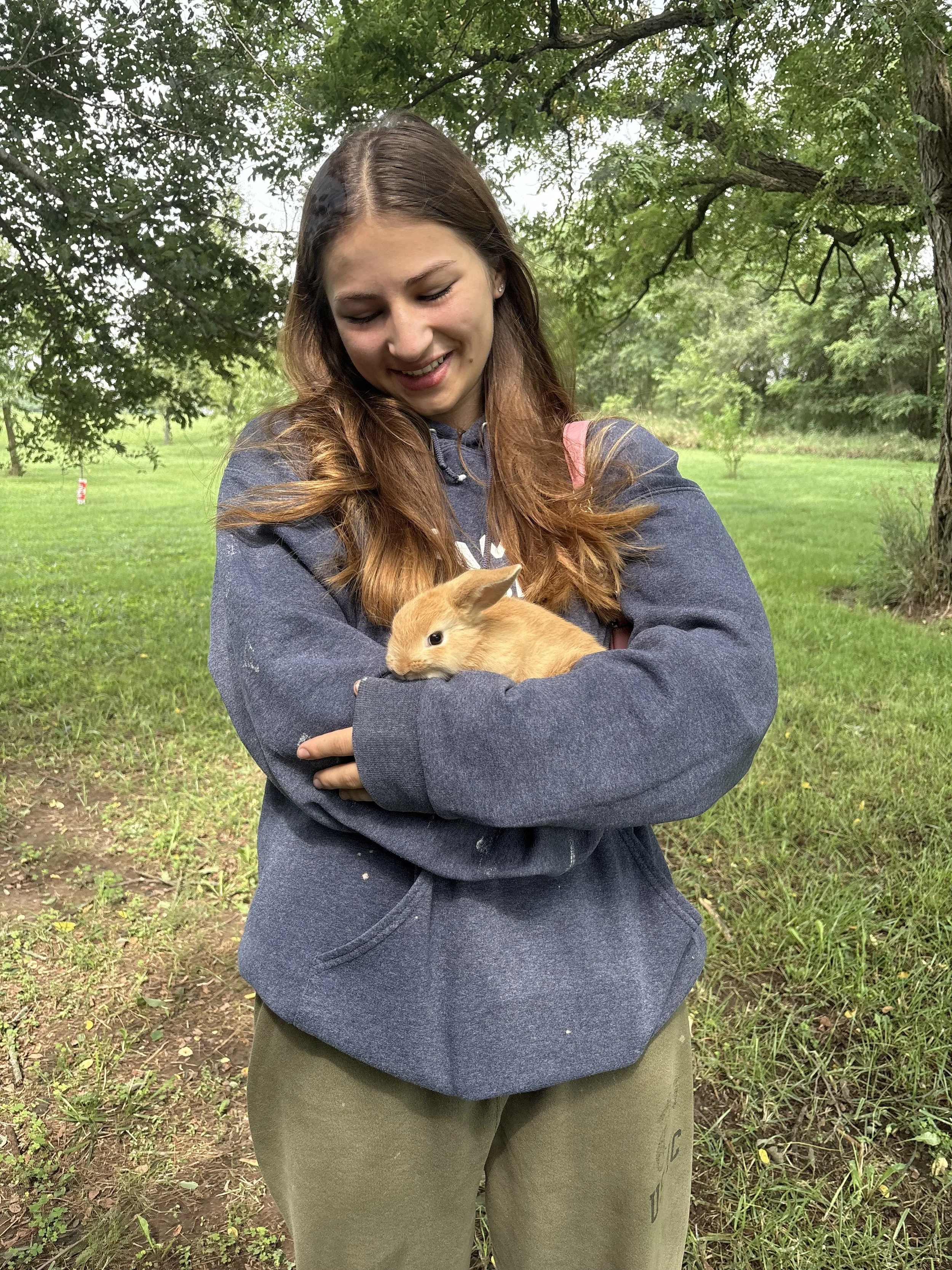 Young woman holding a tan rabbit outdoors in a leafy park