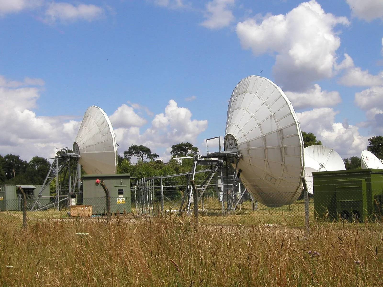 Satellite dishes at a ground station under a partly cloudy blue sky