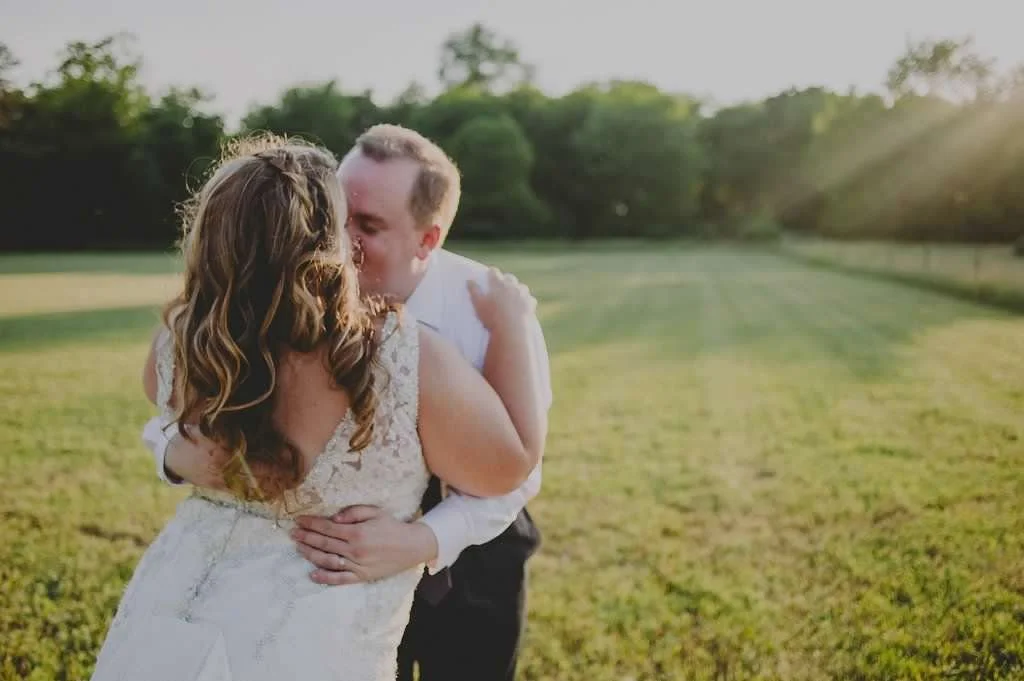 Newlywed couple kissing and embracing in a sunlit field