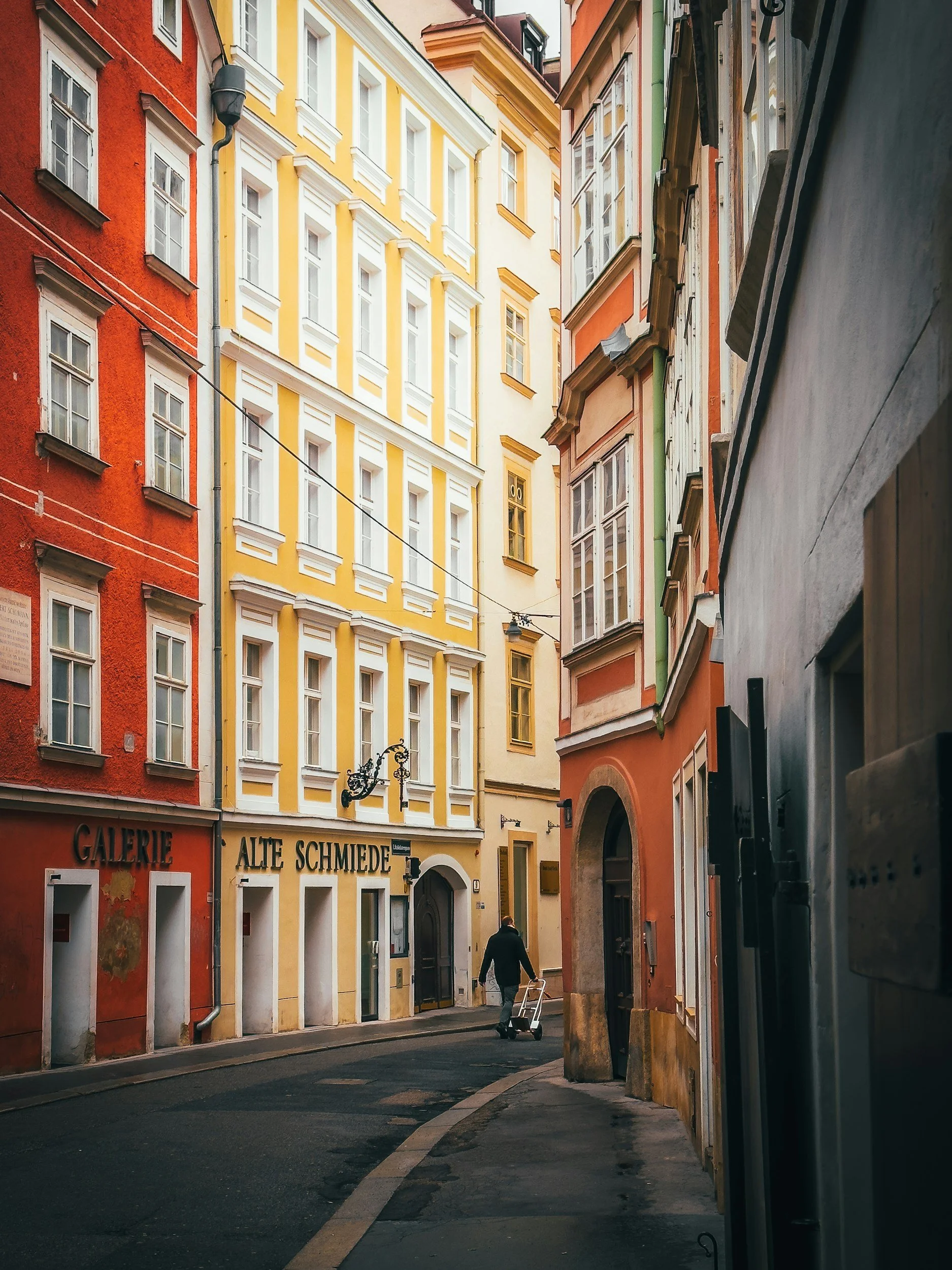 Narrow European street lined with colorful historic buildings and a person pulling a handcart.