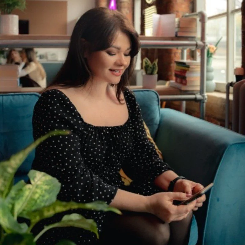 Woman in a black polka-dot dress using a smartphone on a blue sofa