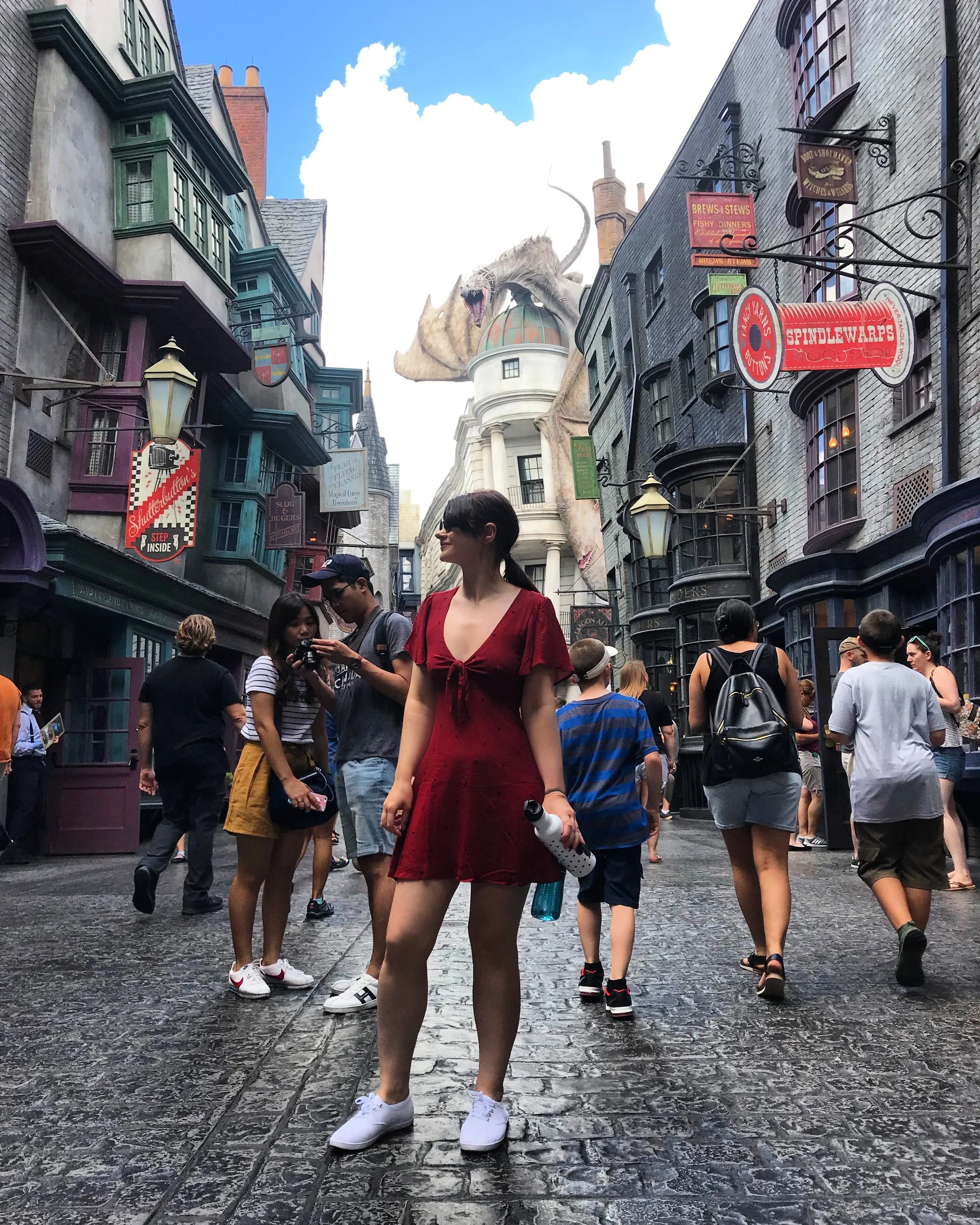 Crowded Diagon Alley at Universal Studios with Hogwarts-themed shops, a large dragon statue, and tourists walking on the cobblestone street.