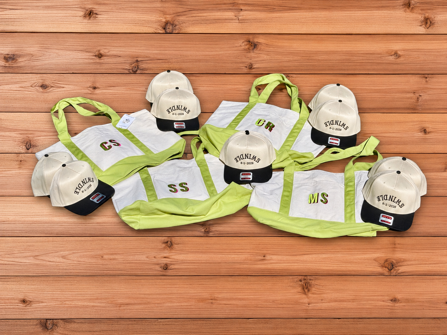 White and neon green tote bags with matching embroidered baseball caps arranged on a wooden background