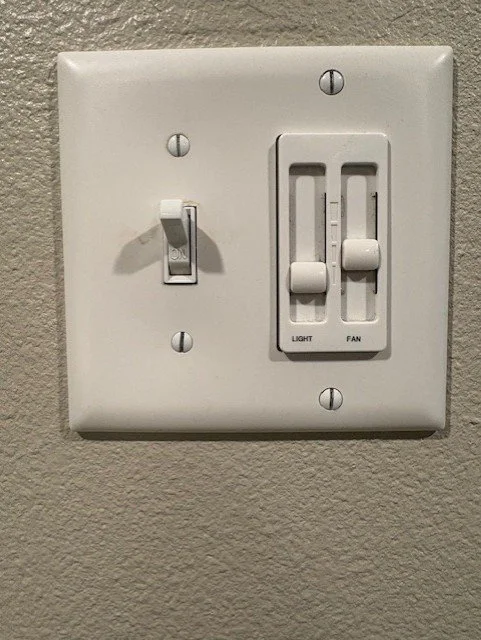 White wall plate with a light switch and separate sliding controls for light and ceiling fan.