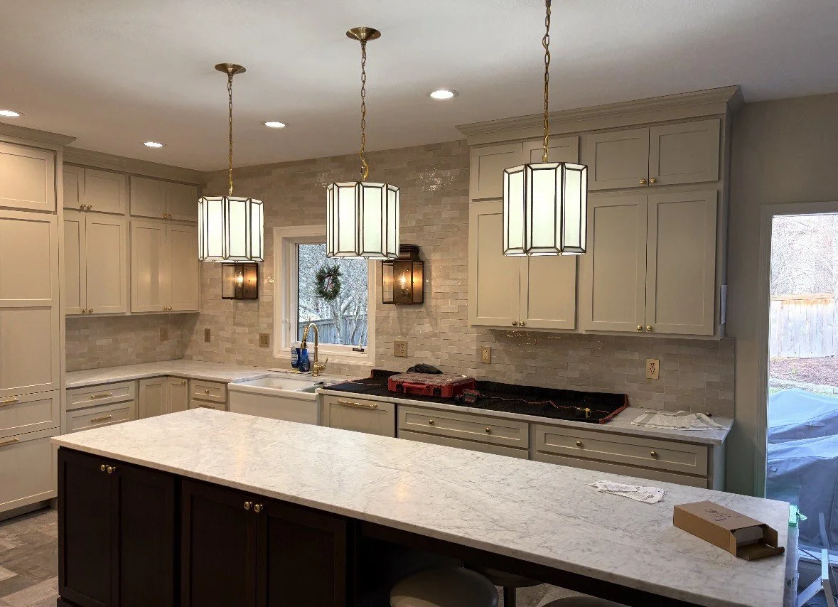 Bright remodeled kitchen with cream cabinets, marble countertops, white subway tile backsplash, large island, and three pendant lights
