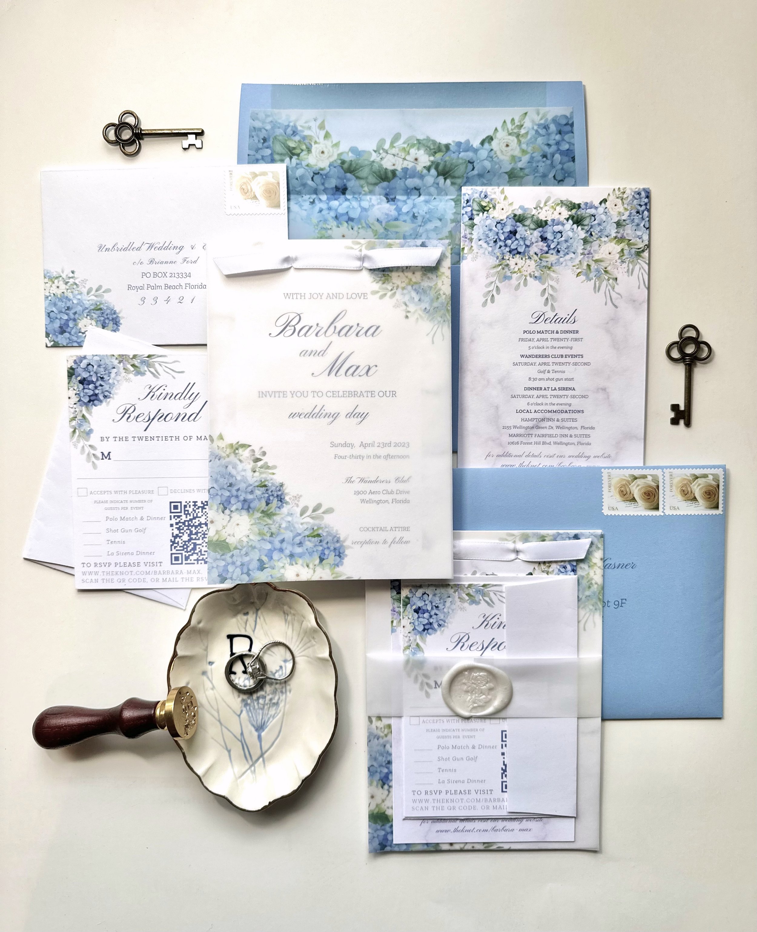 Custom flat-lay of blue hydrangea wedding invitation, with floral details cards, envelopes, wax seal, and ribbon. Detail card, rsvp card, blue envelope, invitation suite