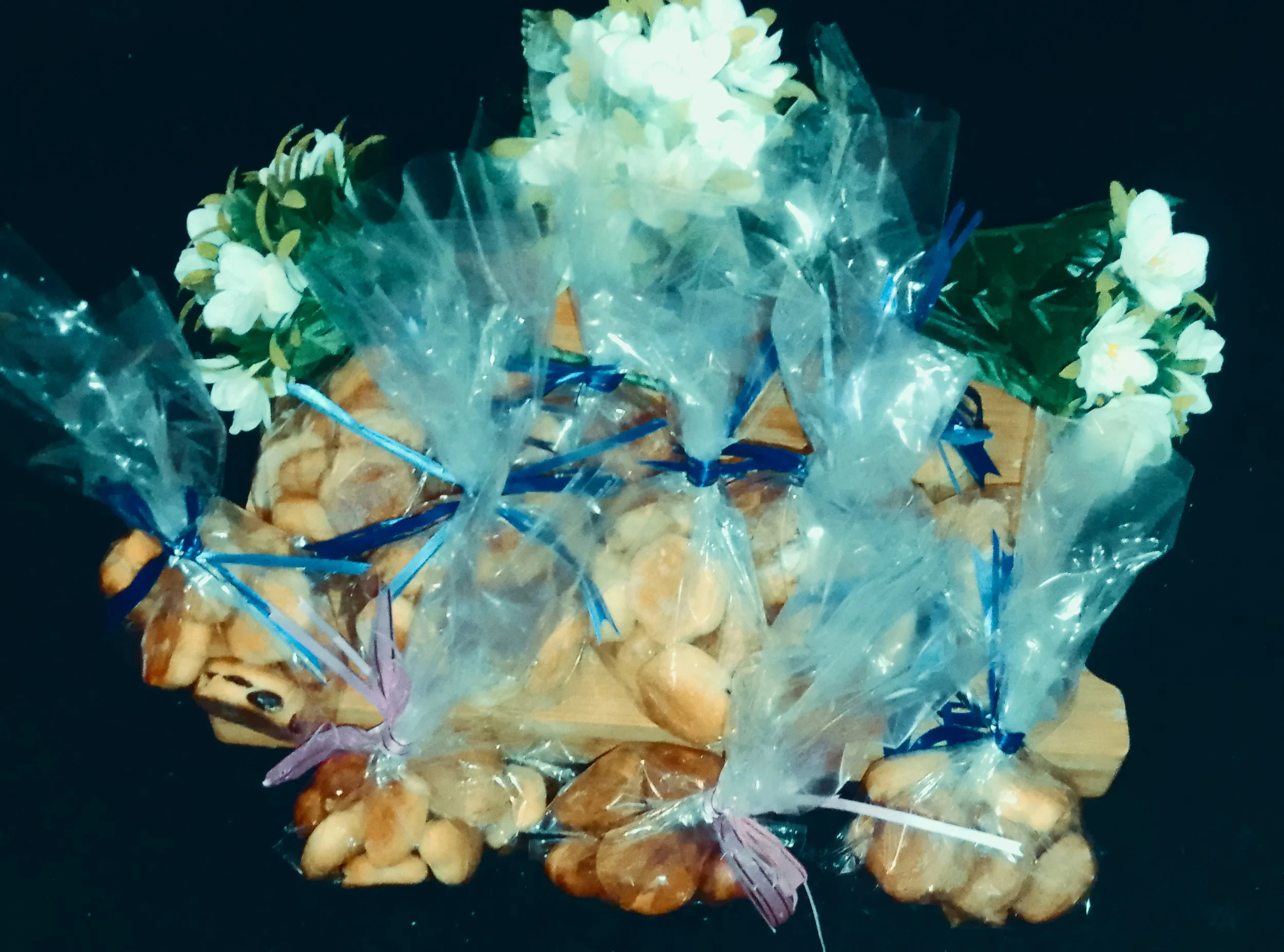 Assortiment de petits pains emballés dans du plastique transparent, décoré de fleurs blanches et de rubans bleus.