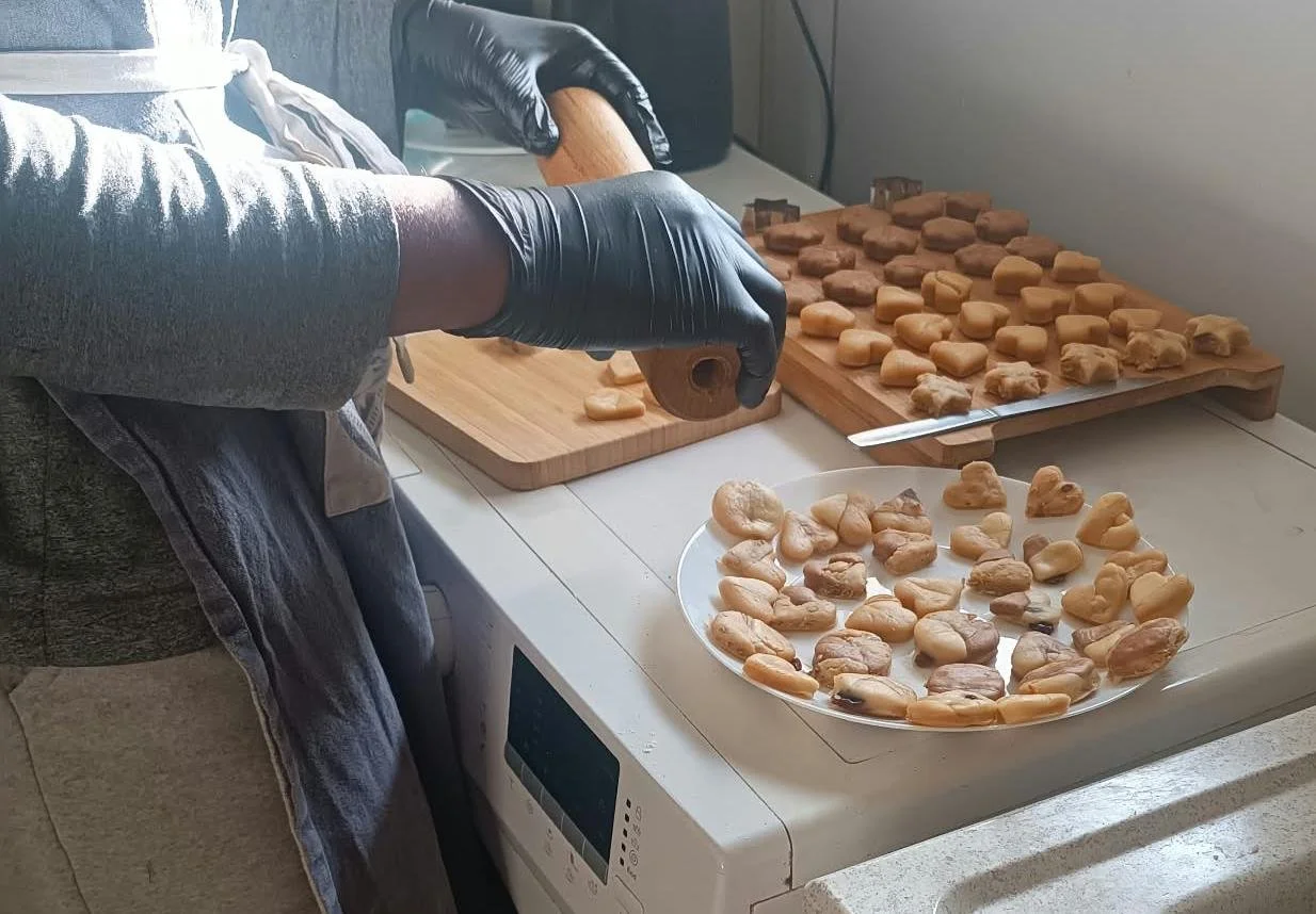 Personne portant des gants noirs préparant de petits morceaux de pâte sur des planches en bois, avec une assiette de bouchées façonnées.