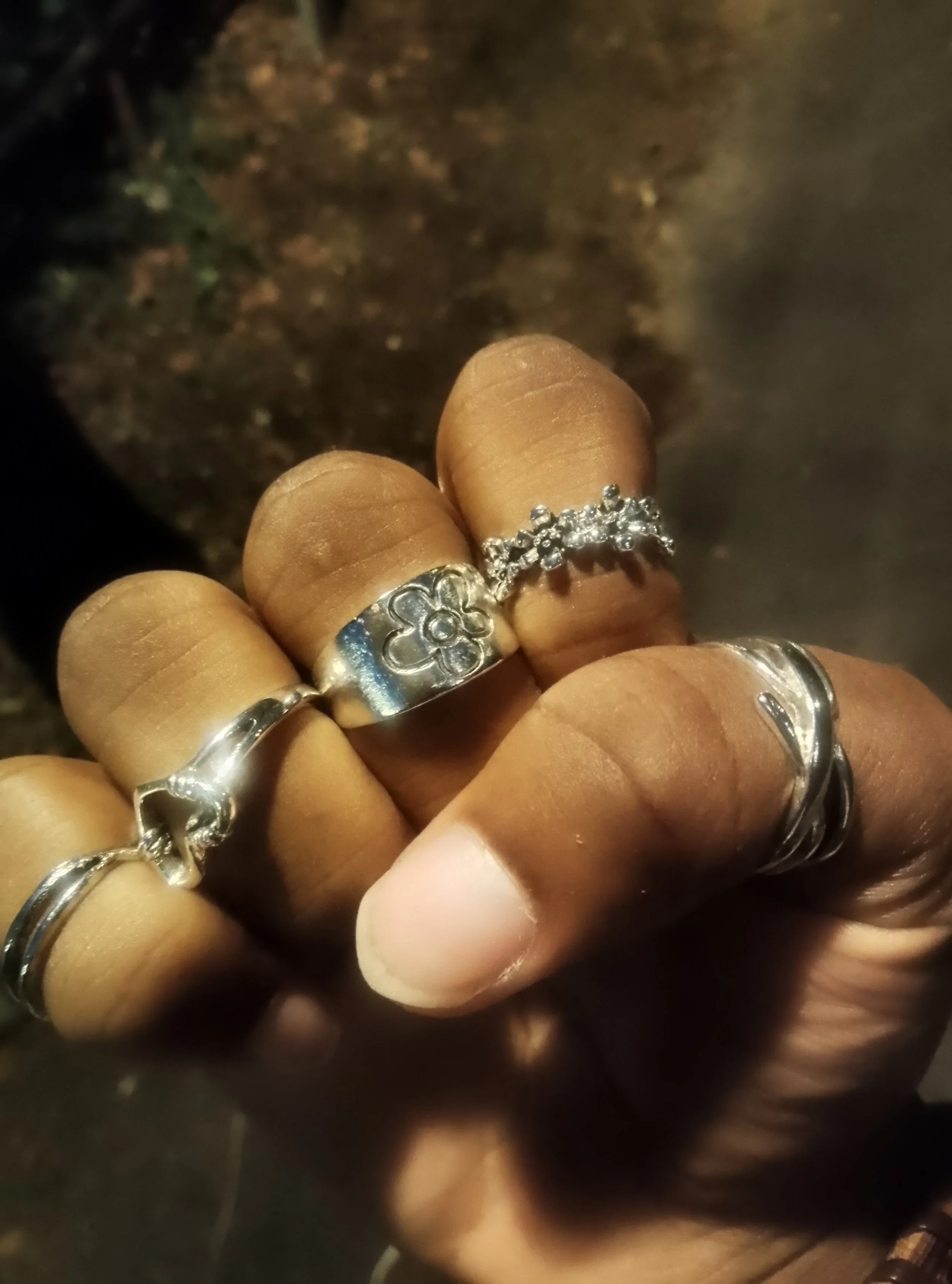 Gros plan sur une main portant plusieurs bagues et bracelets en argent, dont une bague ornée d’une fleur et de pierres bleues.