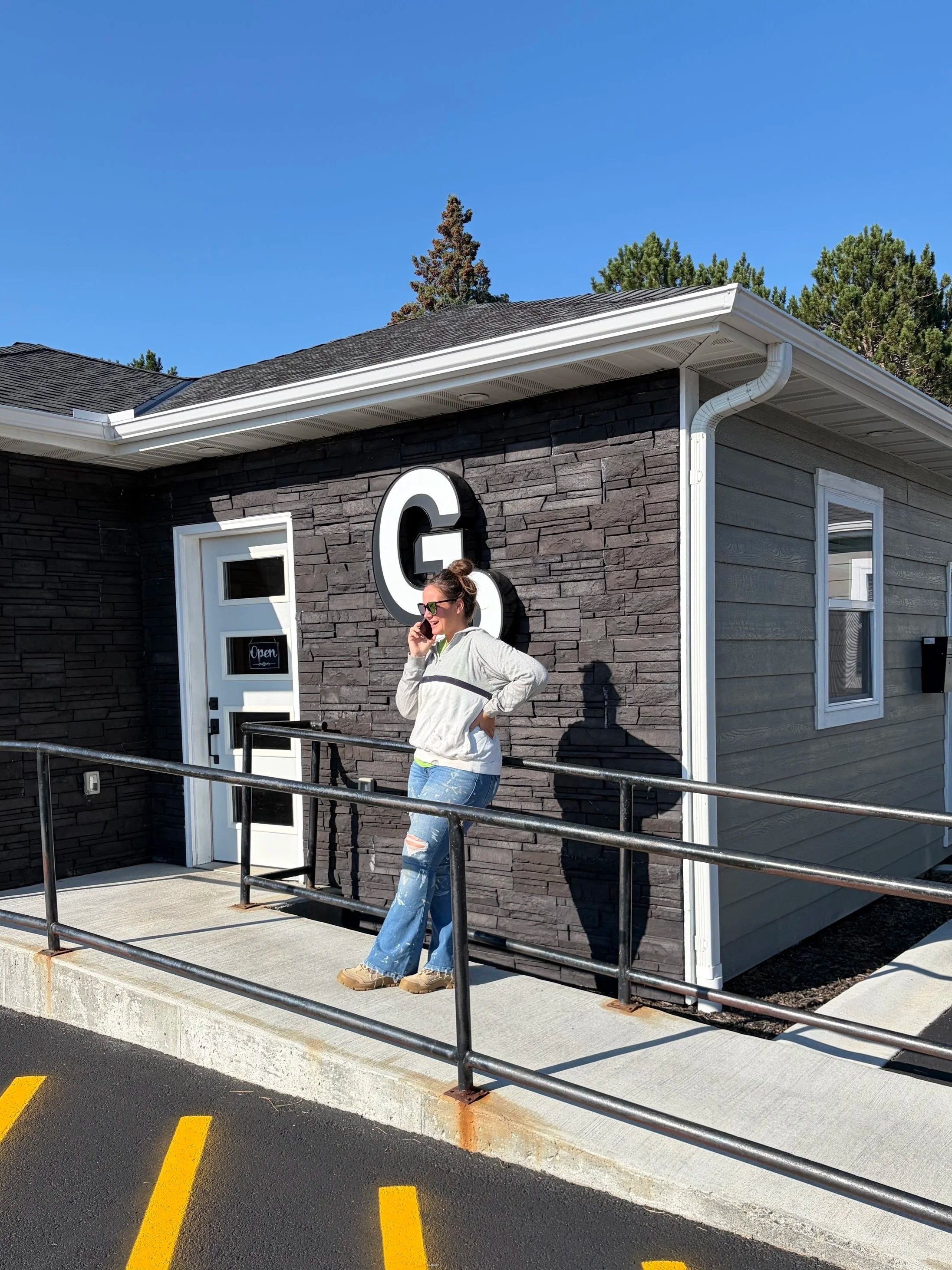 Woman standing outside a building with an open sign, stone facade, and wheelchair-accessible ramp.