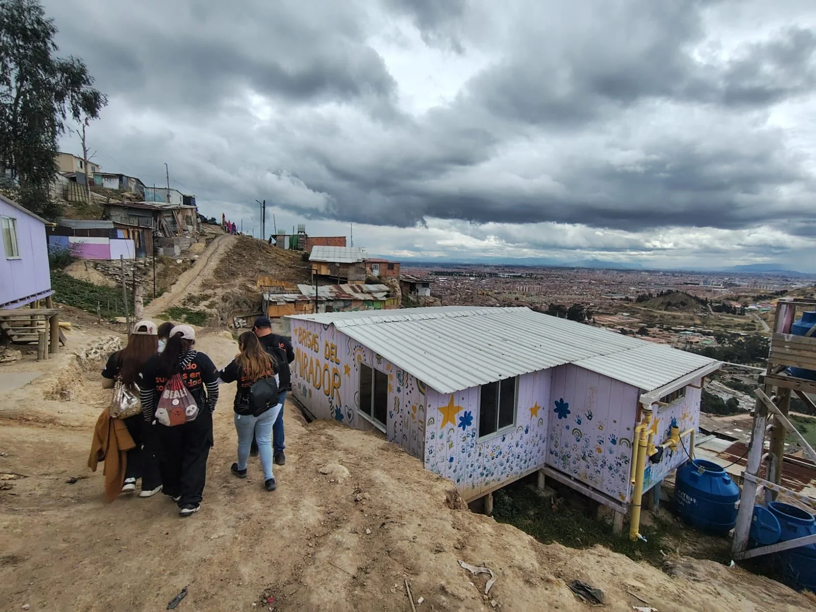 Voluntades caminando por Brisas del Mirador, una de las comunidades en donde interviene Sueños en Red, con una amplia vista de Soacha y Bogotá bajo un cielo nublado.