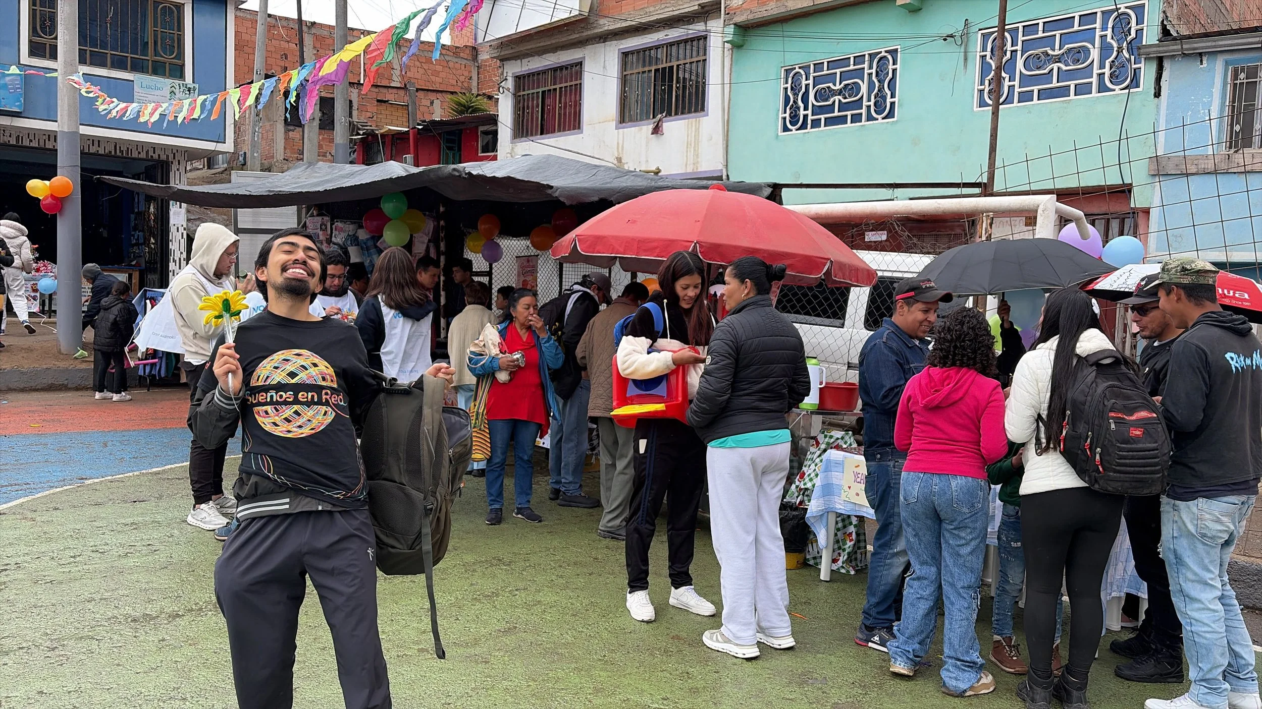Habitantes de El Recuerdo Sur, comunidad de Ciudad Bolívar donde la Fundación interviene, en una feria de emprendimiento al aire libre, con puestos de comida, globos, sombrillas y banderines coloridos.