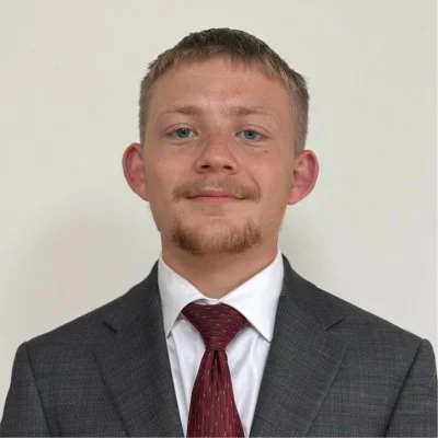 Portrait of a young man wearing a gray suit, white dress shirt, and burgundy tie.