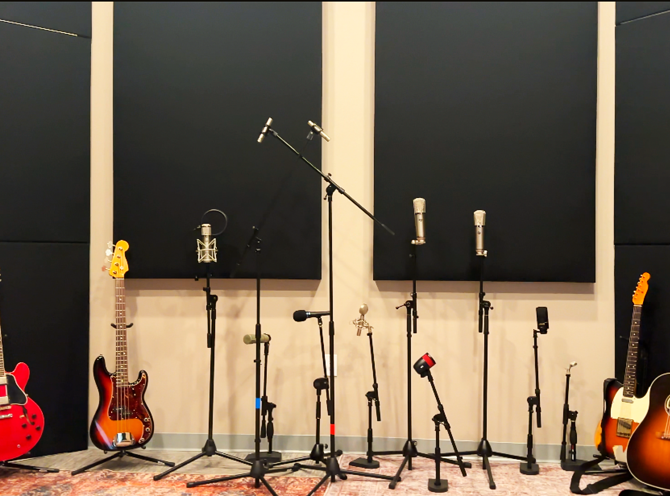 Recording studio with multiple microphones on stands, acoustic panels, electric guitars, and a bass guitar.