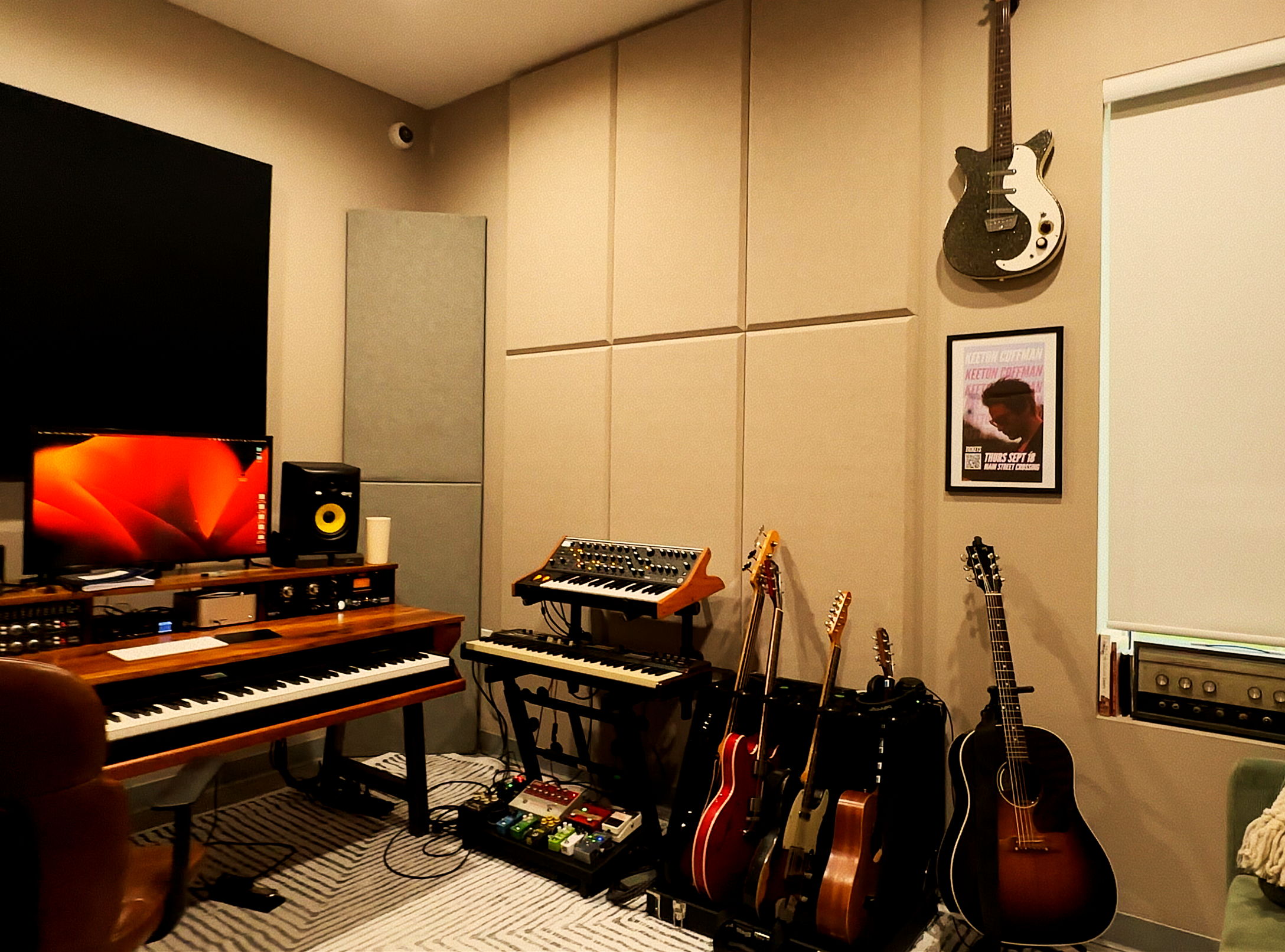Home music studio with keyboards, guitars, audio equipment, studio monitors, and acoustic wall panels.