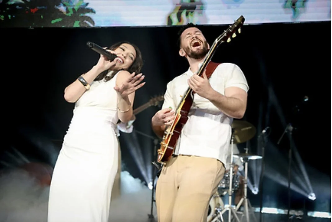 Singer performing beside a guitarist on a concert stage