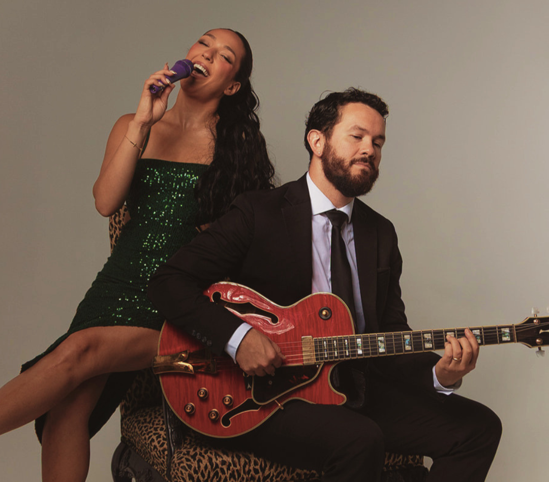 Singer holding a purple microphone behind a man in a suit playing a red electric guitar