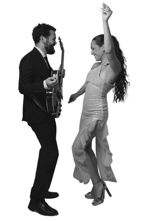 Black-and-white image of a guitarist in a suit playing for a woman dancing in a flowing dress.