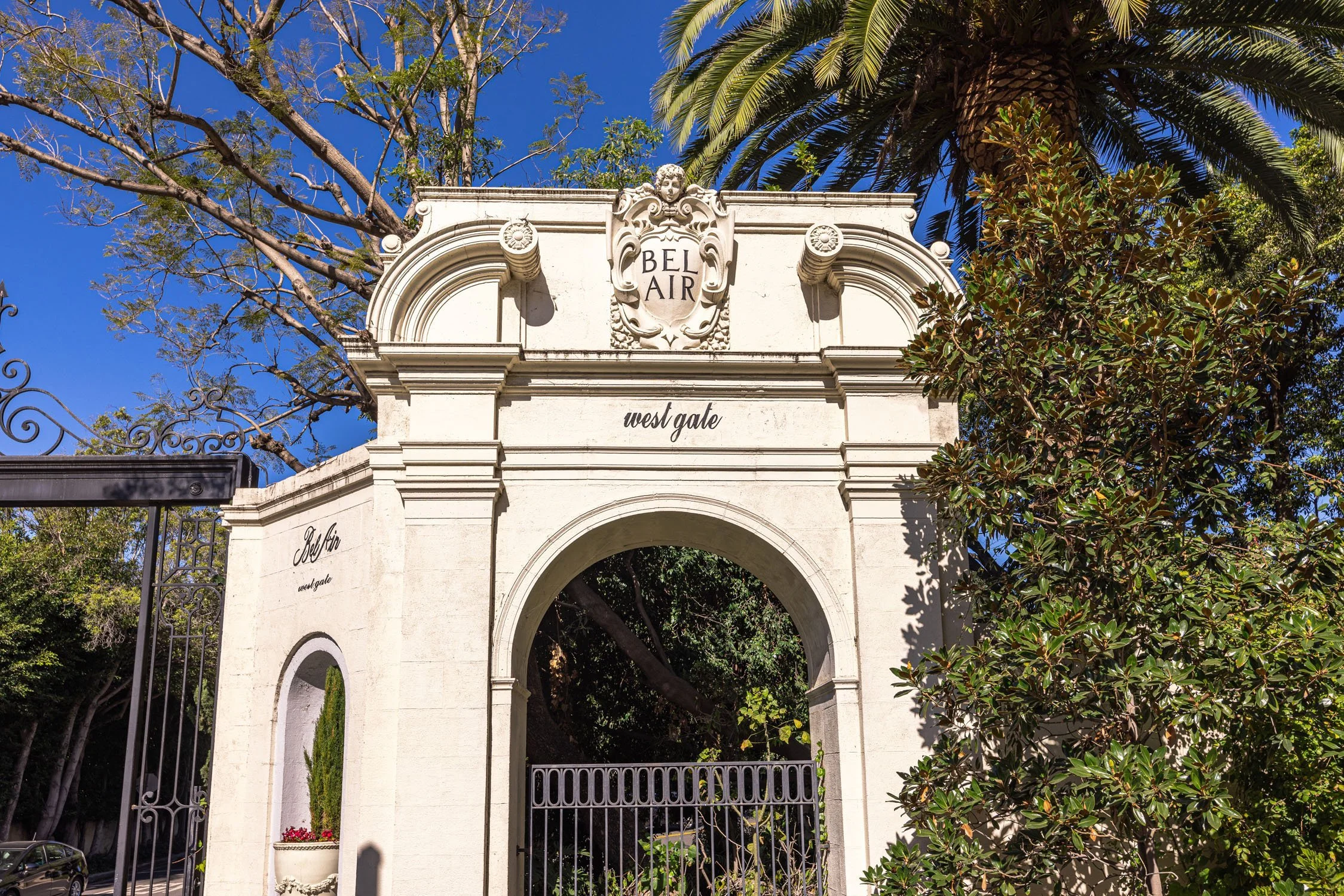 Ornate Bel Air West Gate entrance arch surrounded by palm trees and lush landscaping