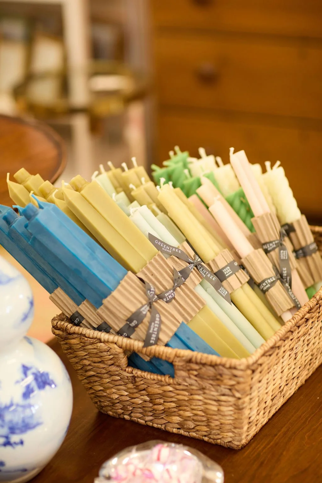 Woven basket filled with colorful GreenTree Home decorative taper candles on a wooden table