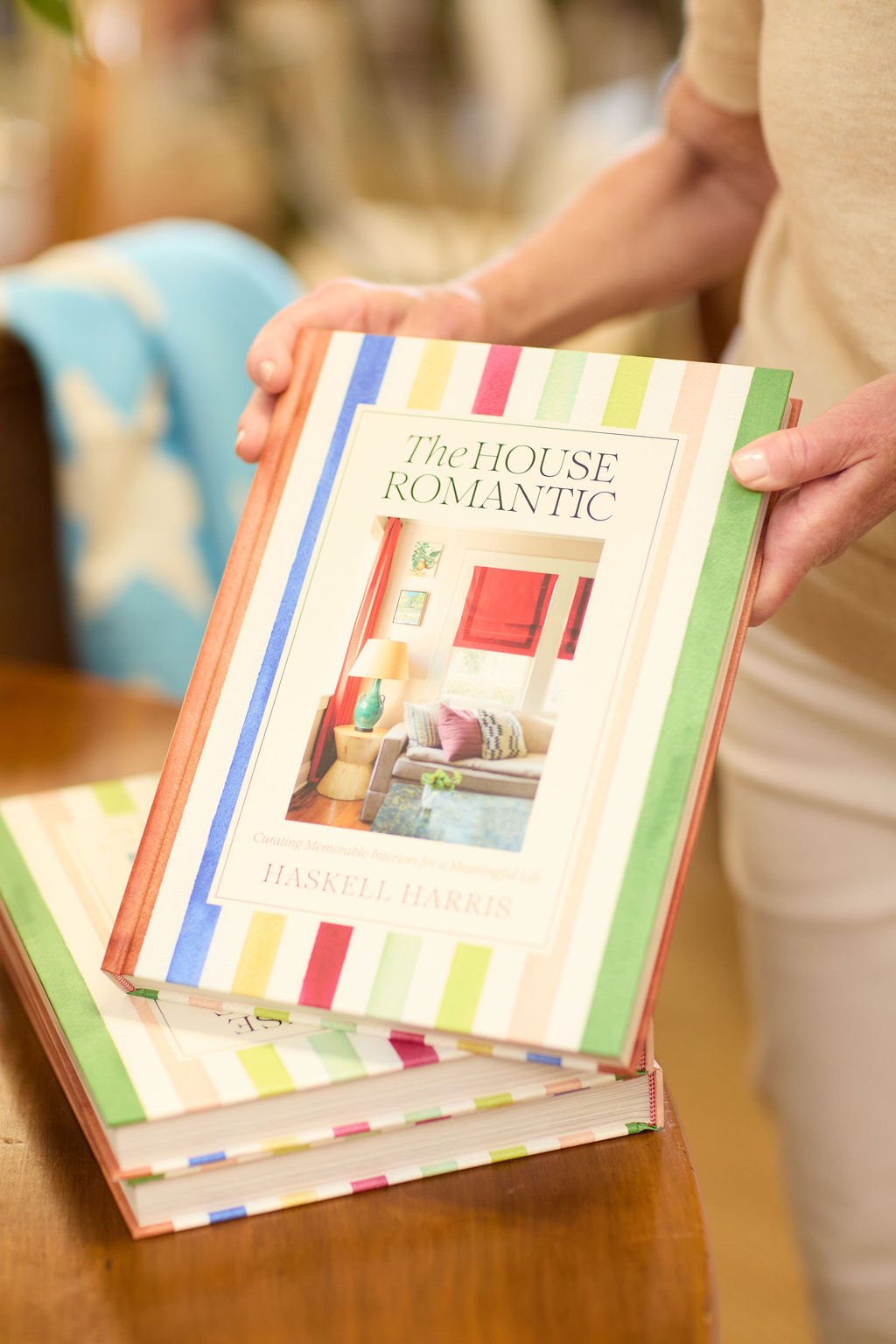Person holding a copy of The House Romantic interior design book above a stack of matching books.