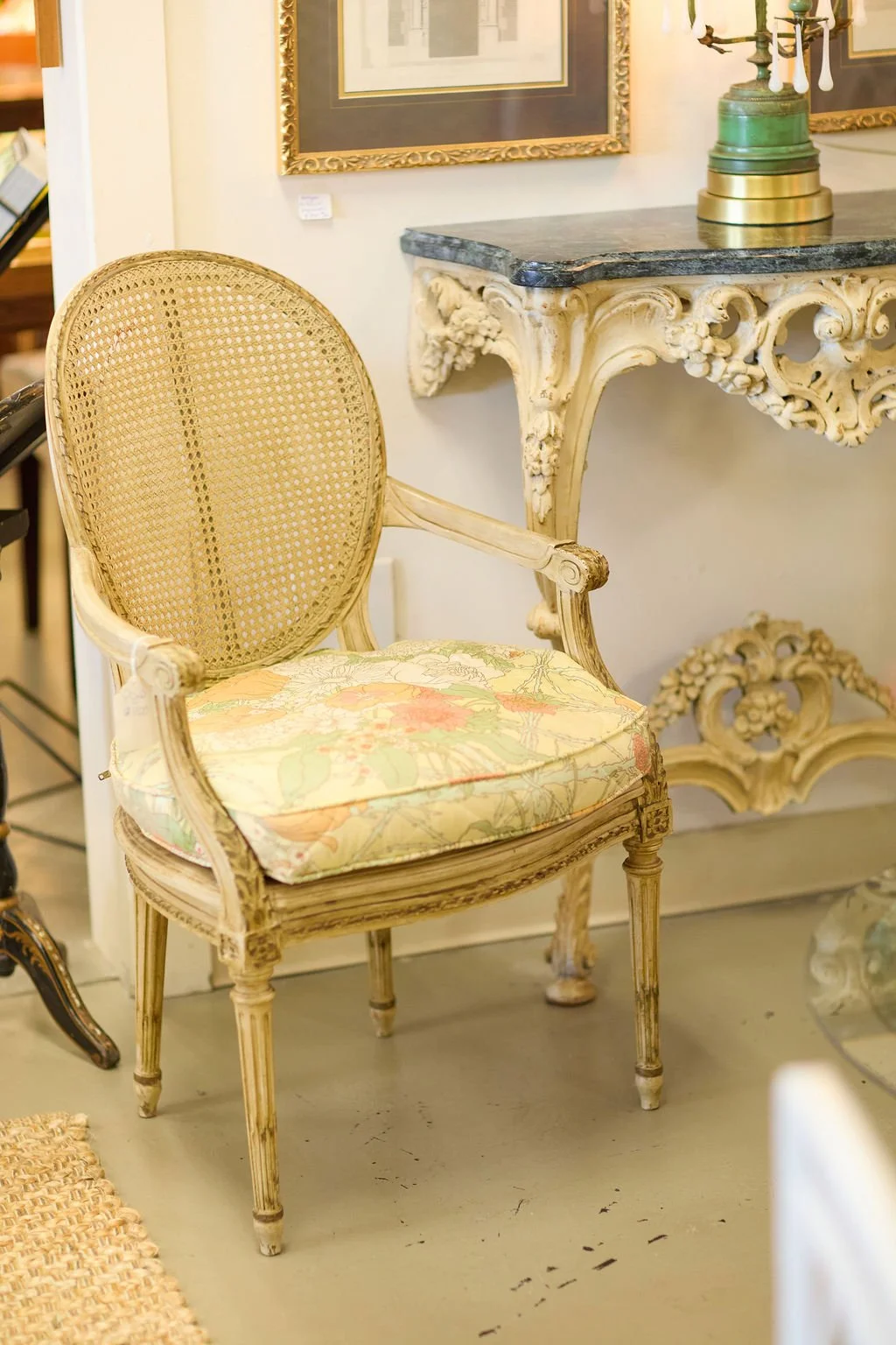 Antique French-style carved wood armchair with cane back and floral upholstered seat beside an ornate gilded console table
