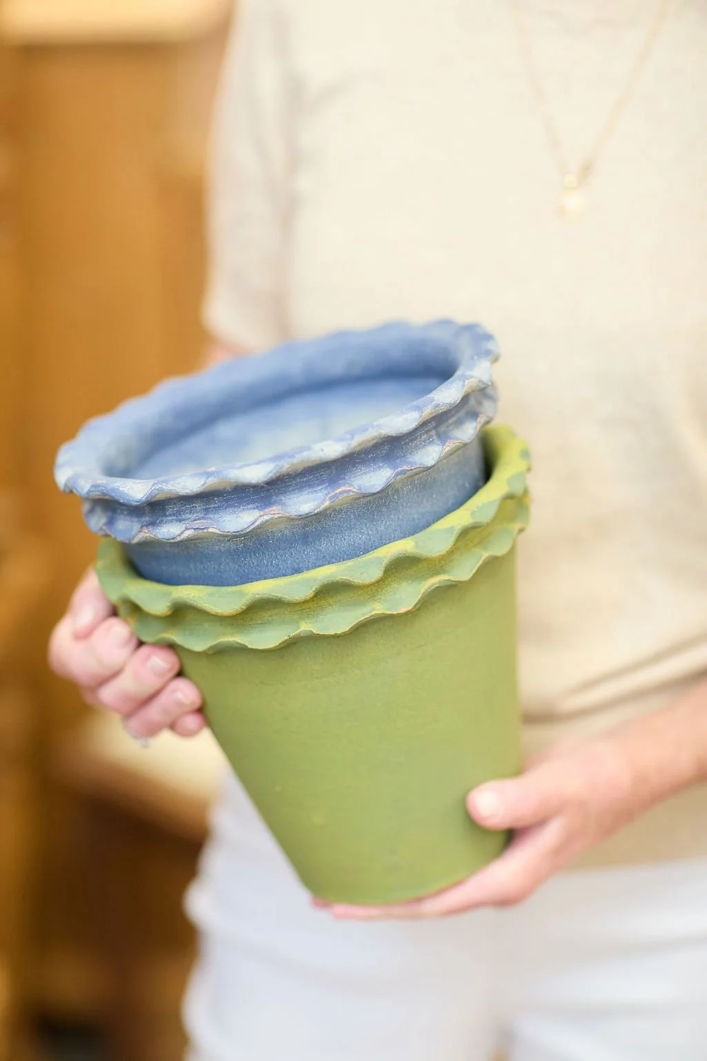 Person holding stacked green and blue ceramic plant pots with scalloped edges