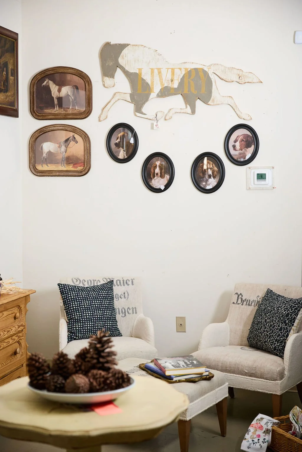 Cozy sitting room with horse and dog artwork, two upholstered armchairs, coffee table with pinecones, and books